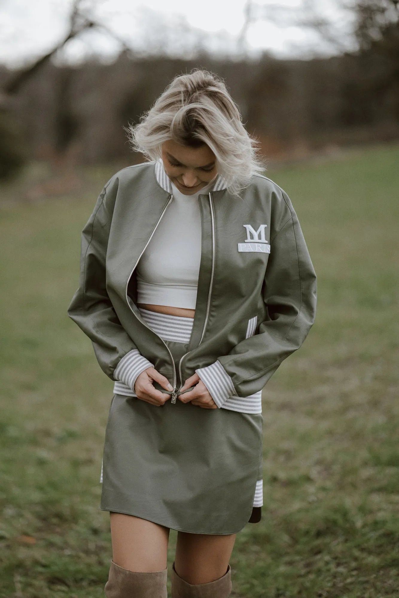 A woman wearing a green bomber jacket and knee-high boots, showcasing a 90s style from Mimaussy Paris.