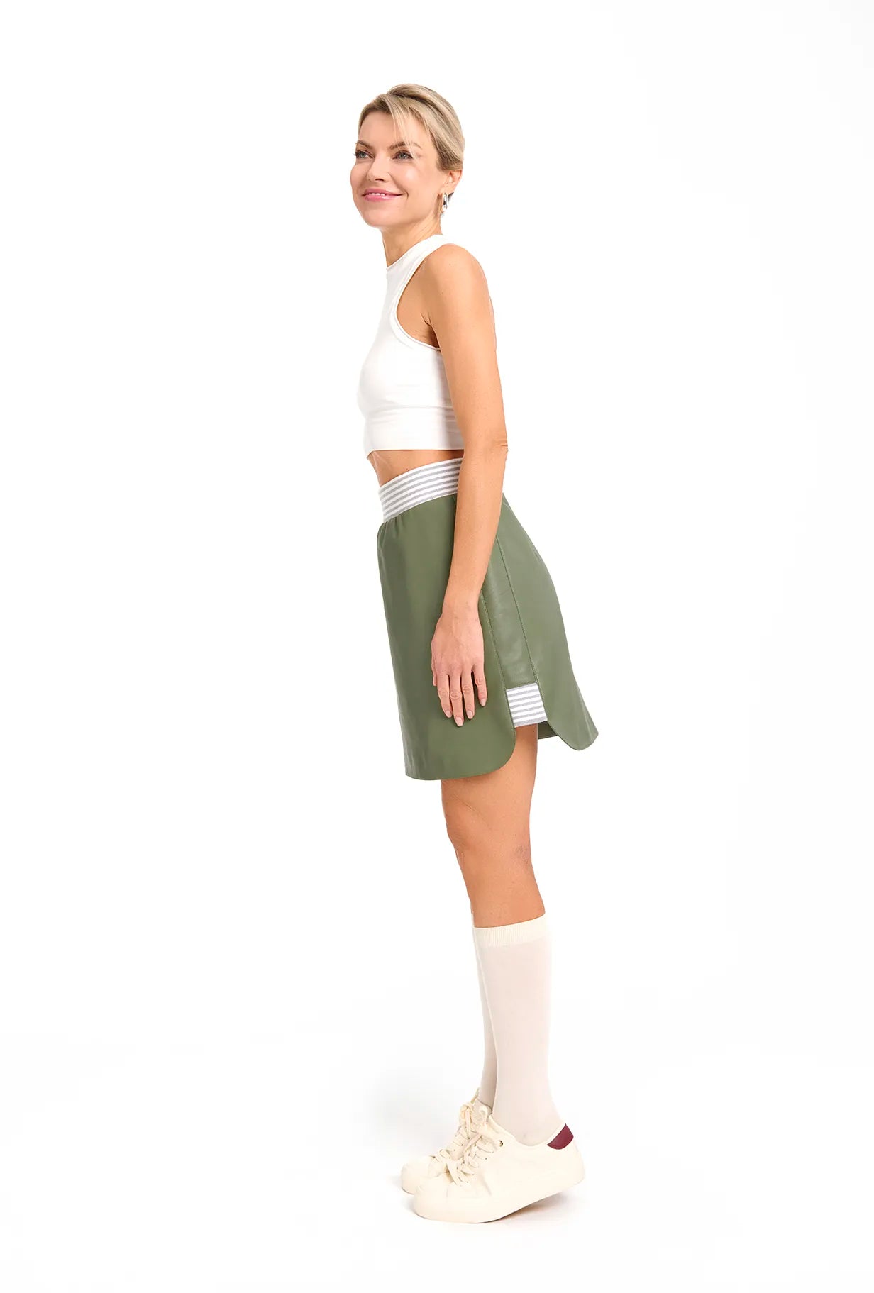 A woman dressed in a white top and a green skirt from Mimaussy Paris, reflecting 90s fashion trends.