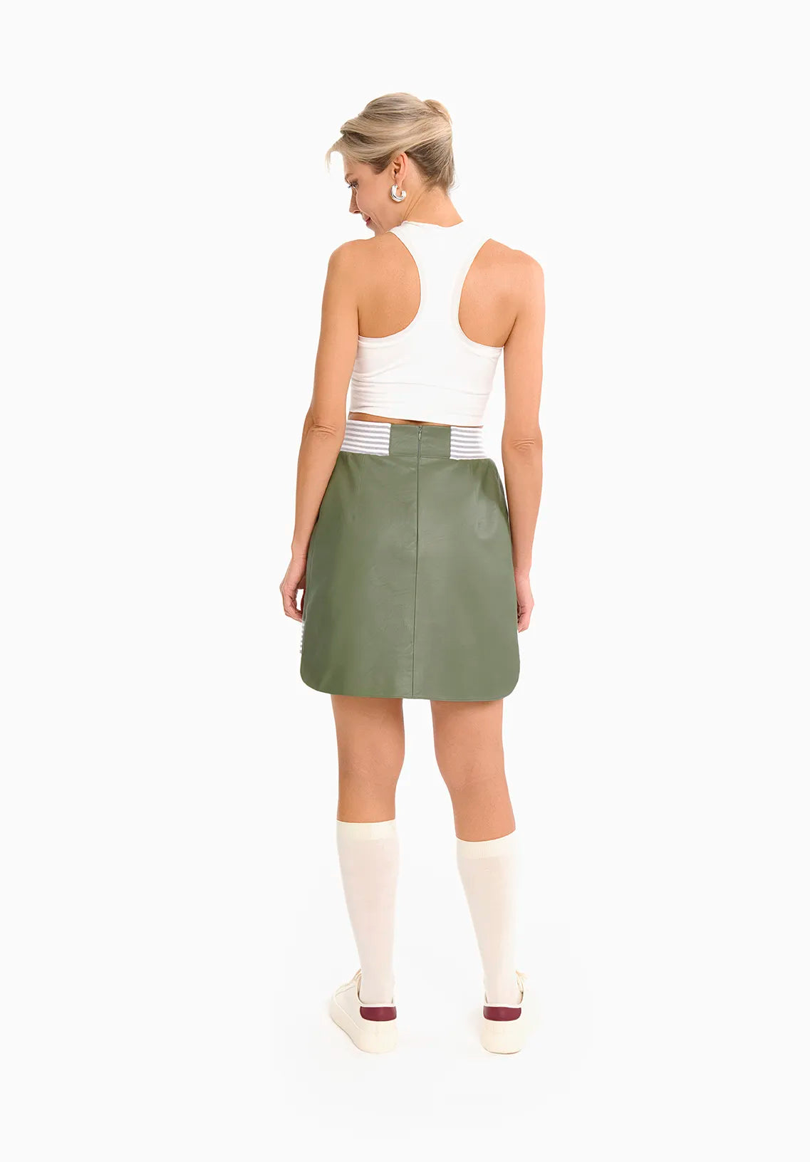 A woman in a white tank top paired with a green Mimaussy Paris 90s style skirt poses elegantly, highlighting her fashion choice.