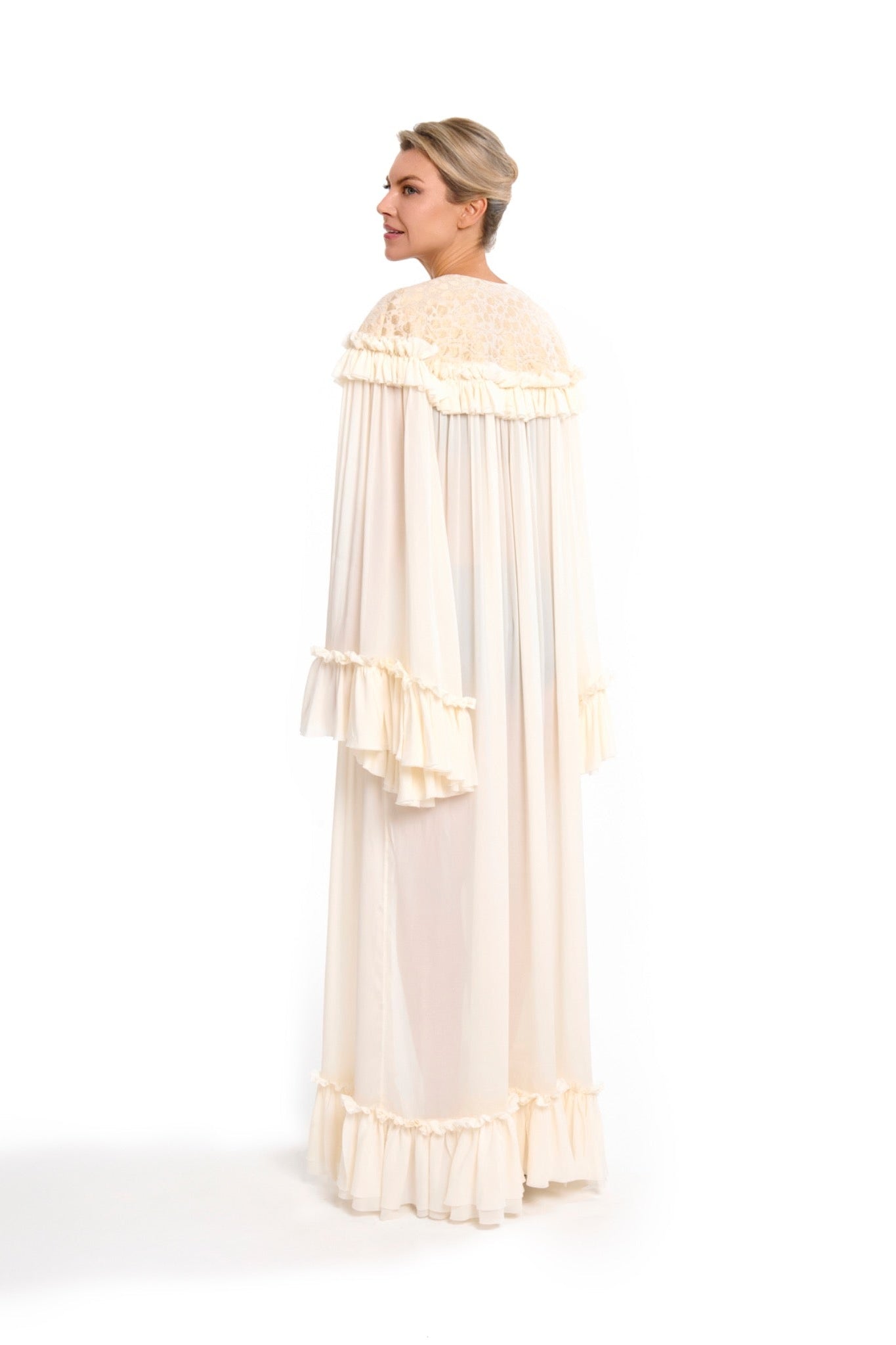 Woman wearing a long, light-colored dress with ruffled details on a white background
