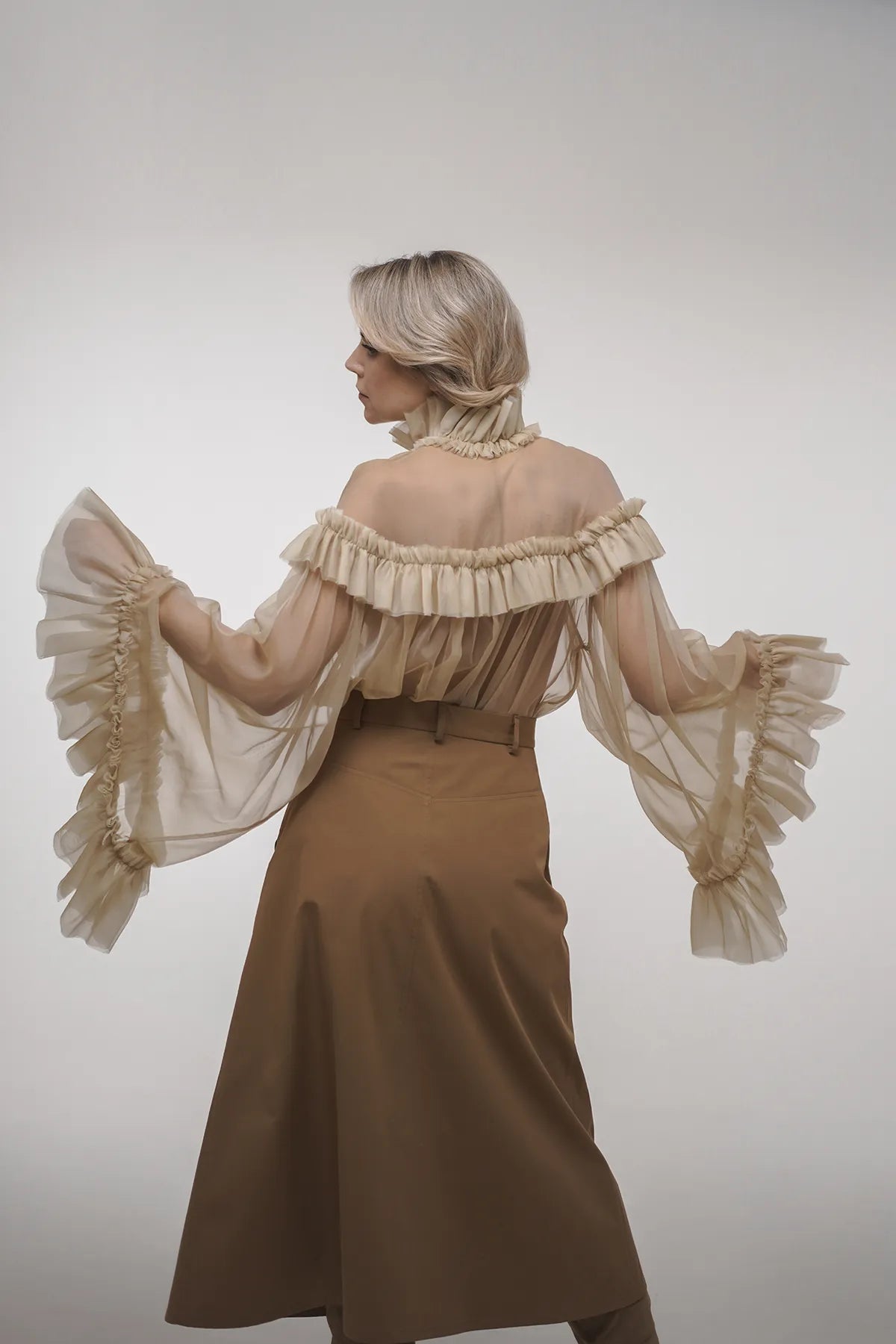 A woman wearing a beige off-the-shoulder dress with an A-line skirt featuring vintage fabric inserts in toffee glaze.