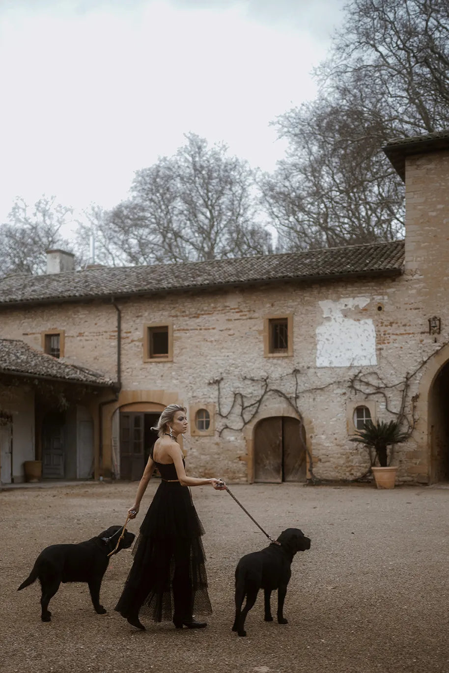 A woman wearing a black Souflé Skirt from Mimaussy Paris strolls with two dogs, enjoying a pleasant day outside.