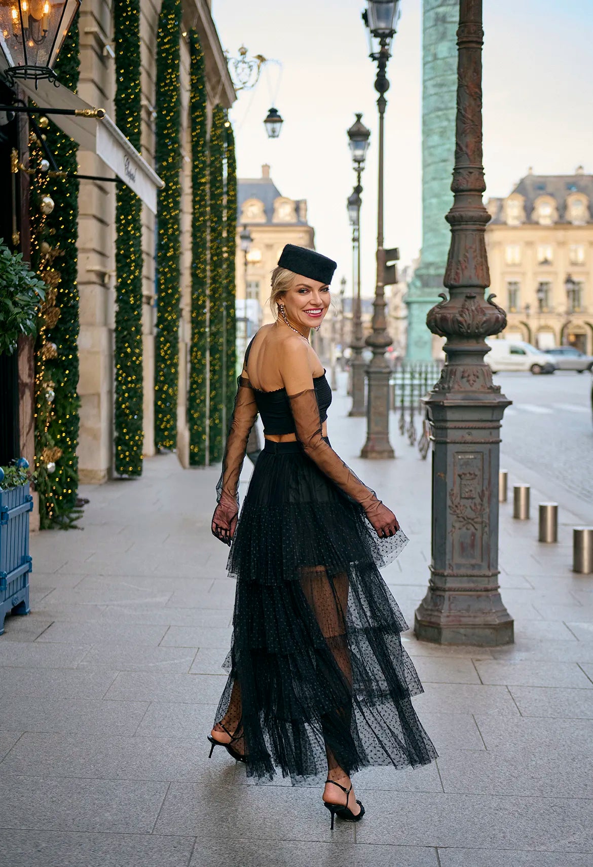A woman in a black dress and hat walks down a Prague street, wearing a Souflé Skirt in Phantom Black from Mimaussy Paris.