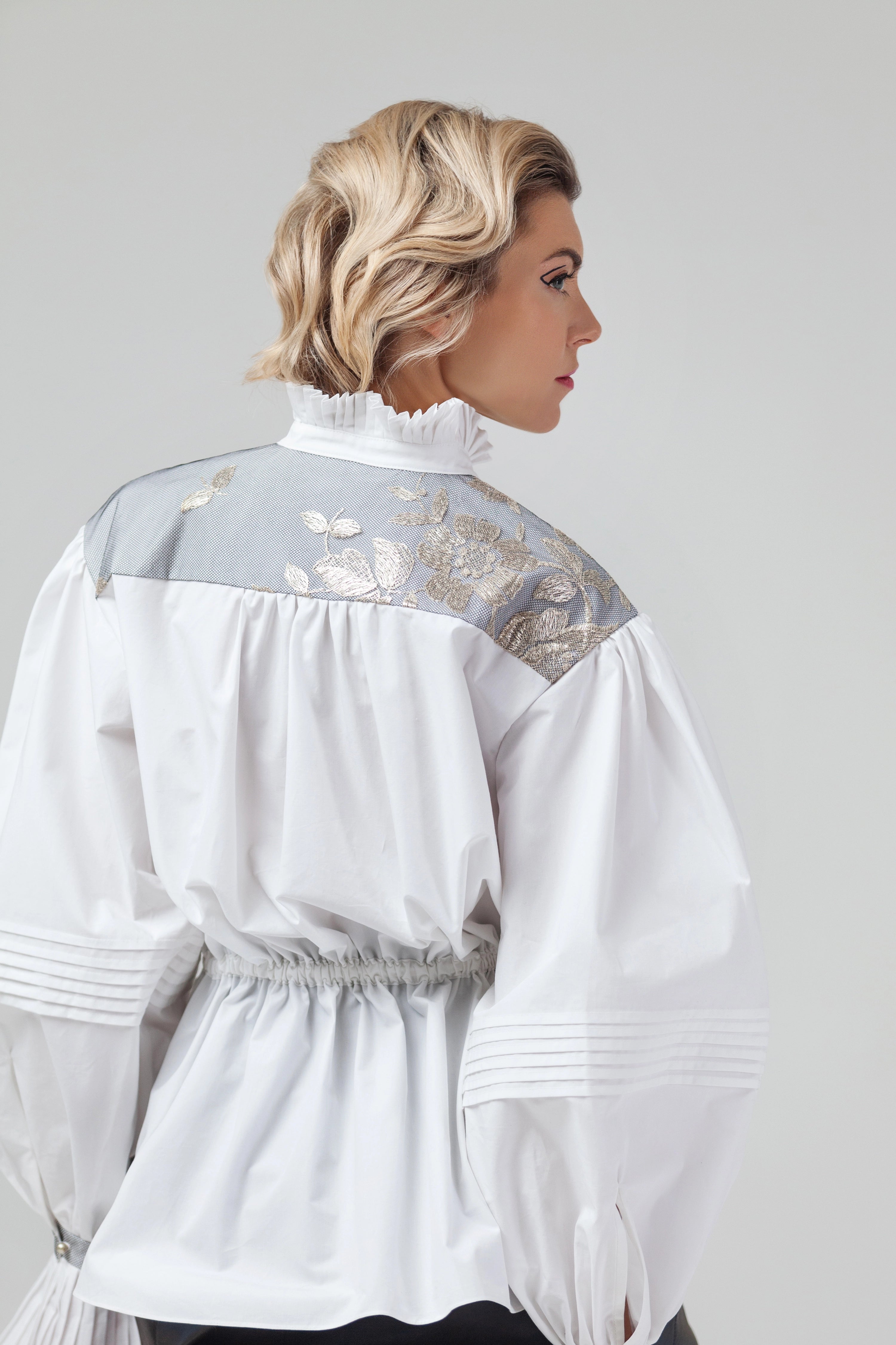 Woman wearing Blanc de Pouvoir from Mimaussy Paris, back view of white blouse with intricate detailing on plain background, studio setting
