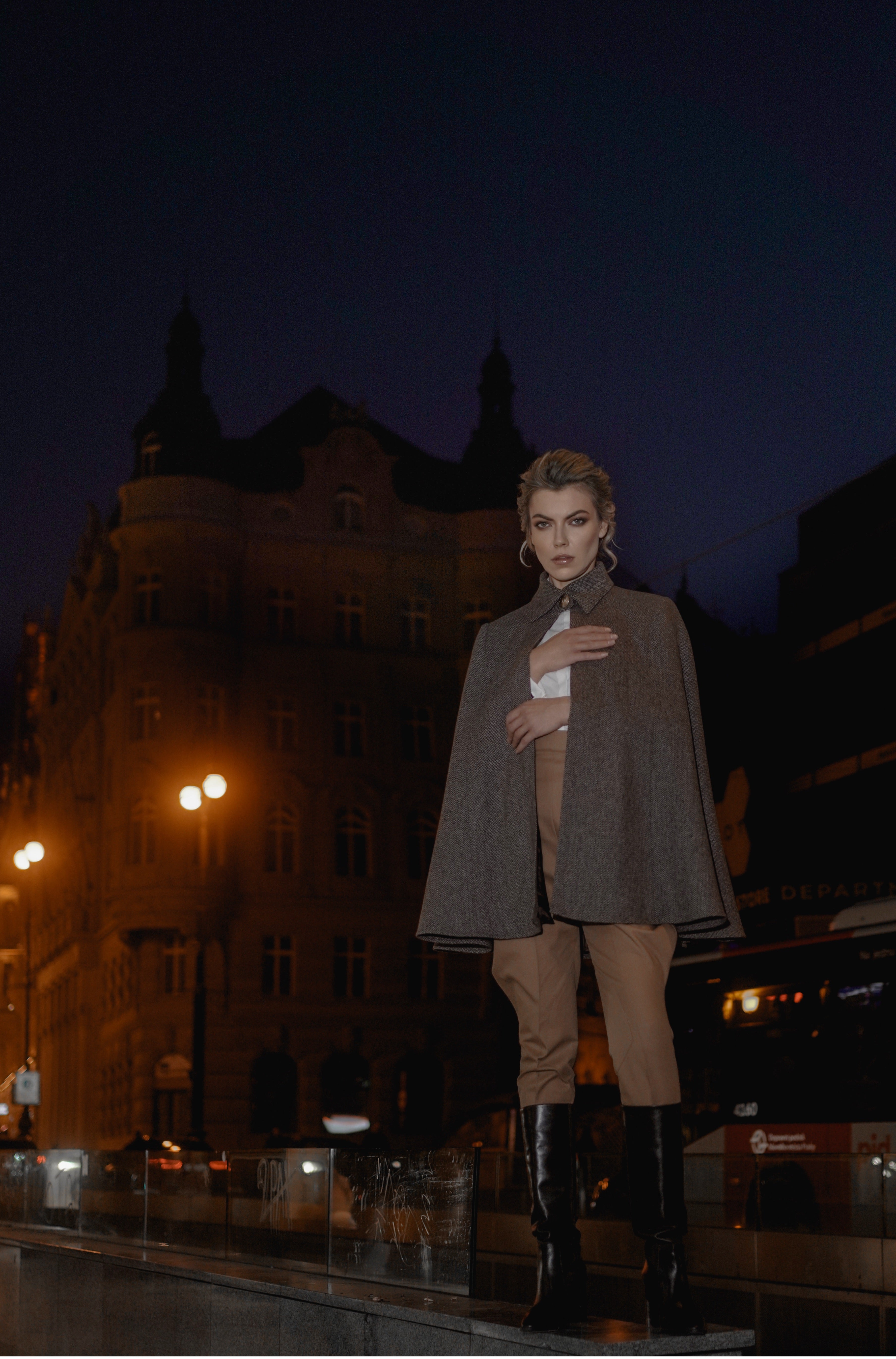 Woman wearing Cape “Brume” from Mimaussy Paris, gray coat standing on street at night with buildings in background outdoors