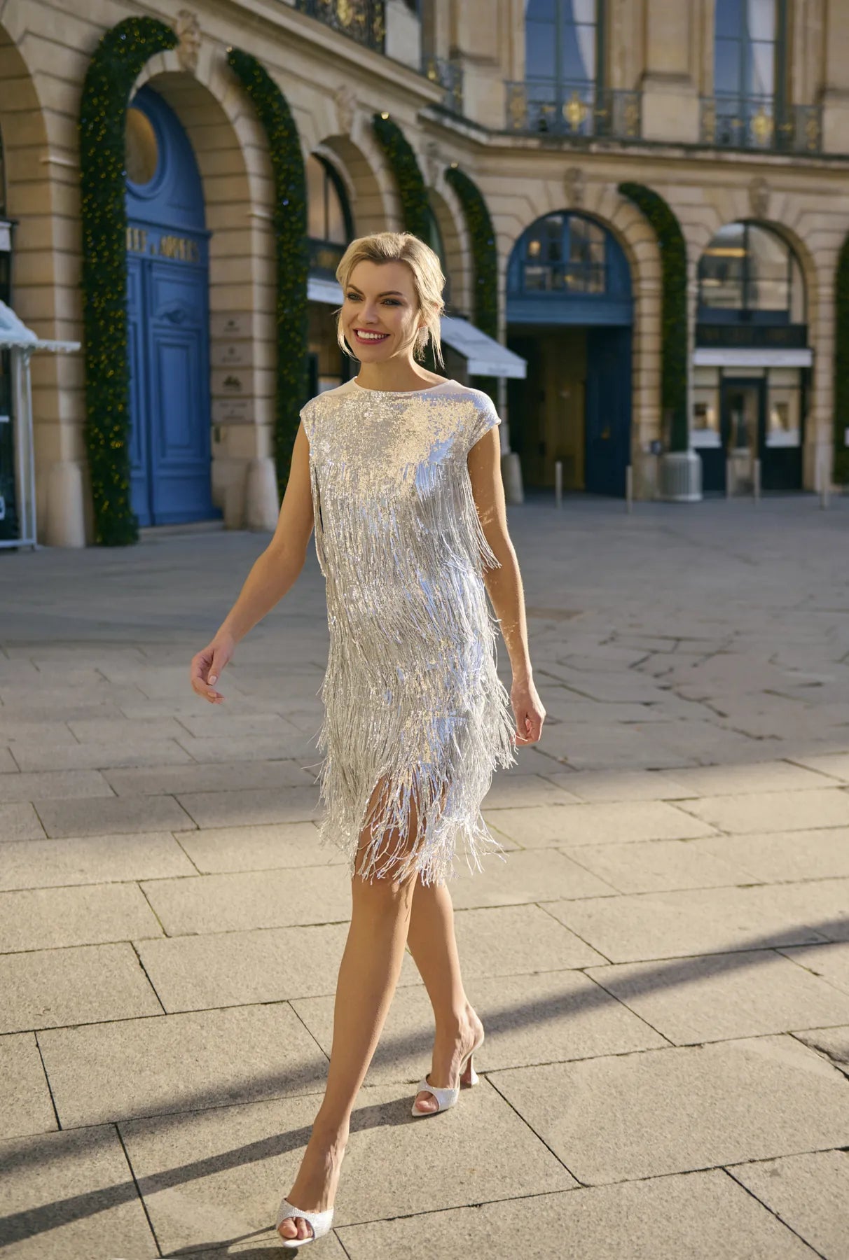 A woman in a shimmering silver dress walks on a street, highlighting the Charleston Glow Top&Skirt Set from Mimaussy Paris.
