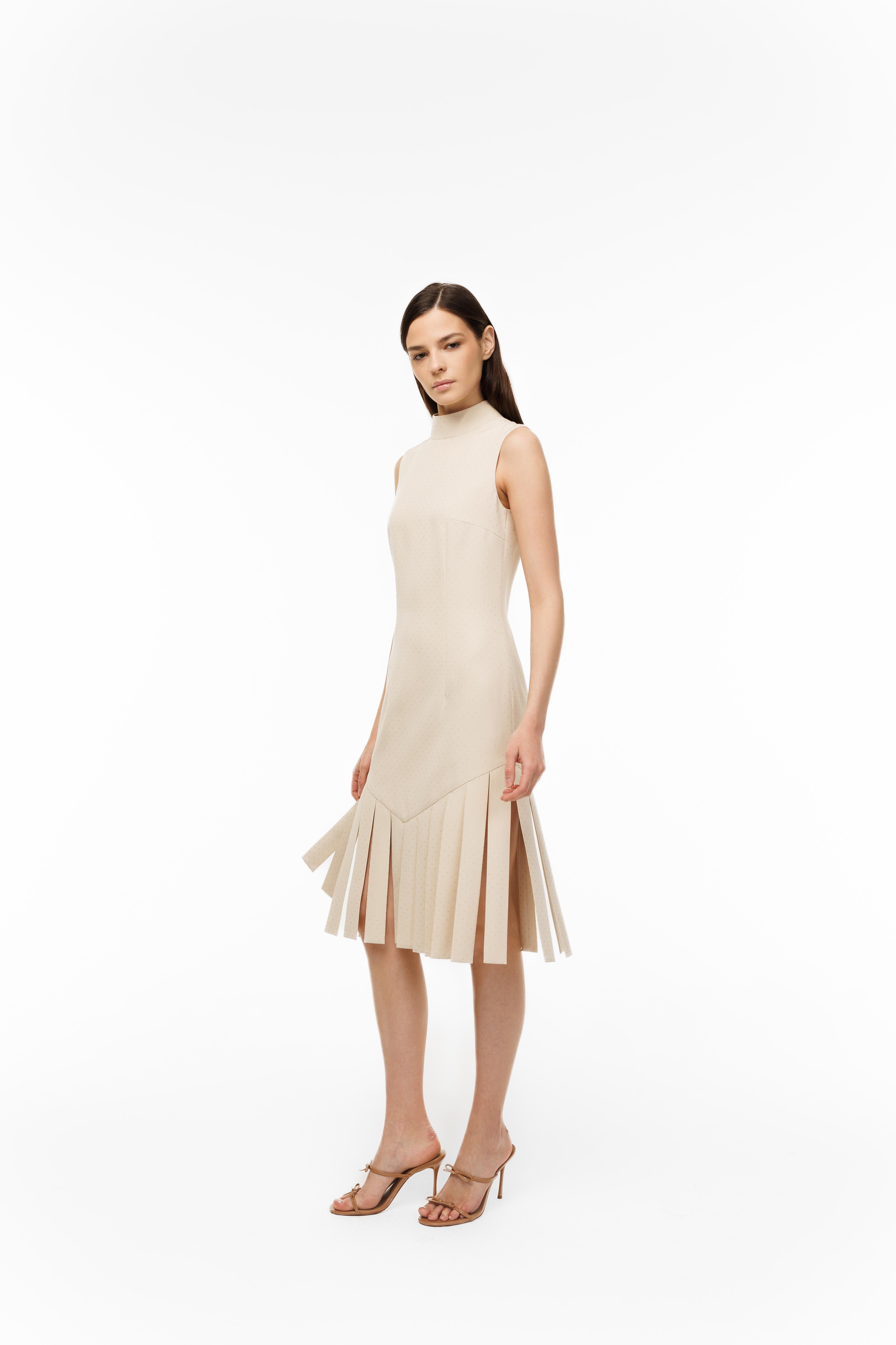 Woman wearing a beige sleeveless dress with pleated skirt on a white background