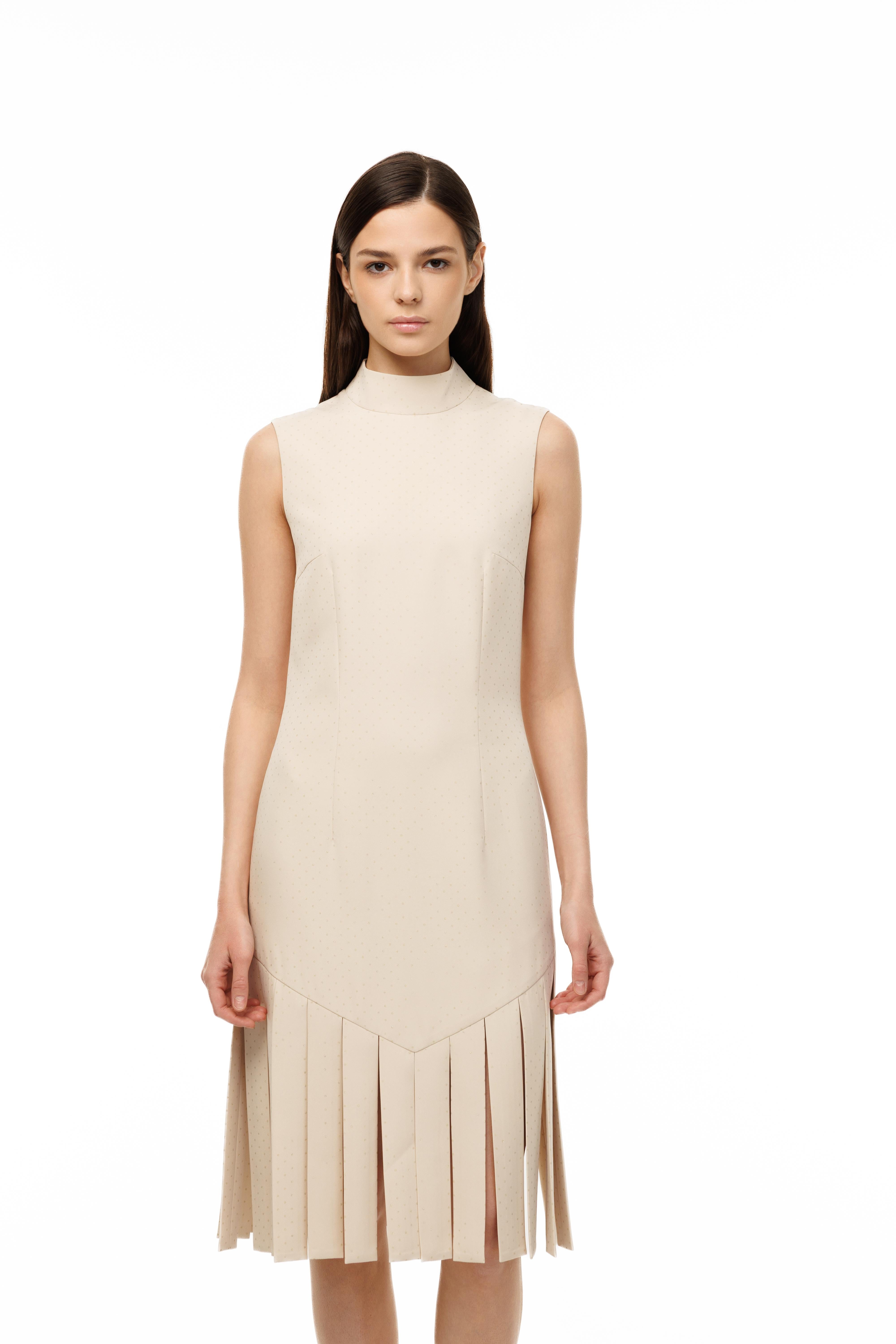 Woman wearing a beige sleeveless dress with pleated skirt on a white background