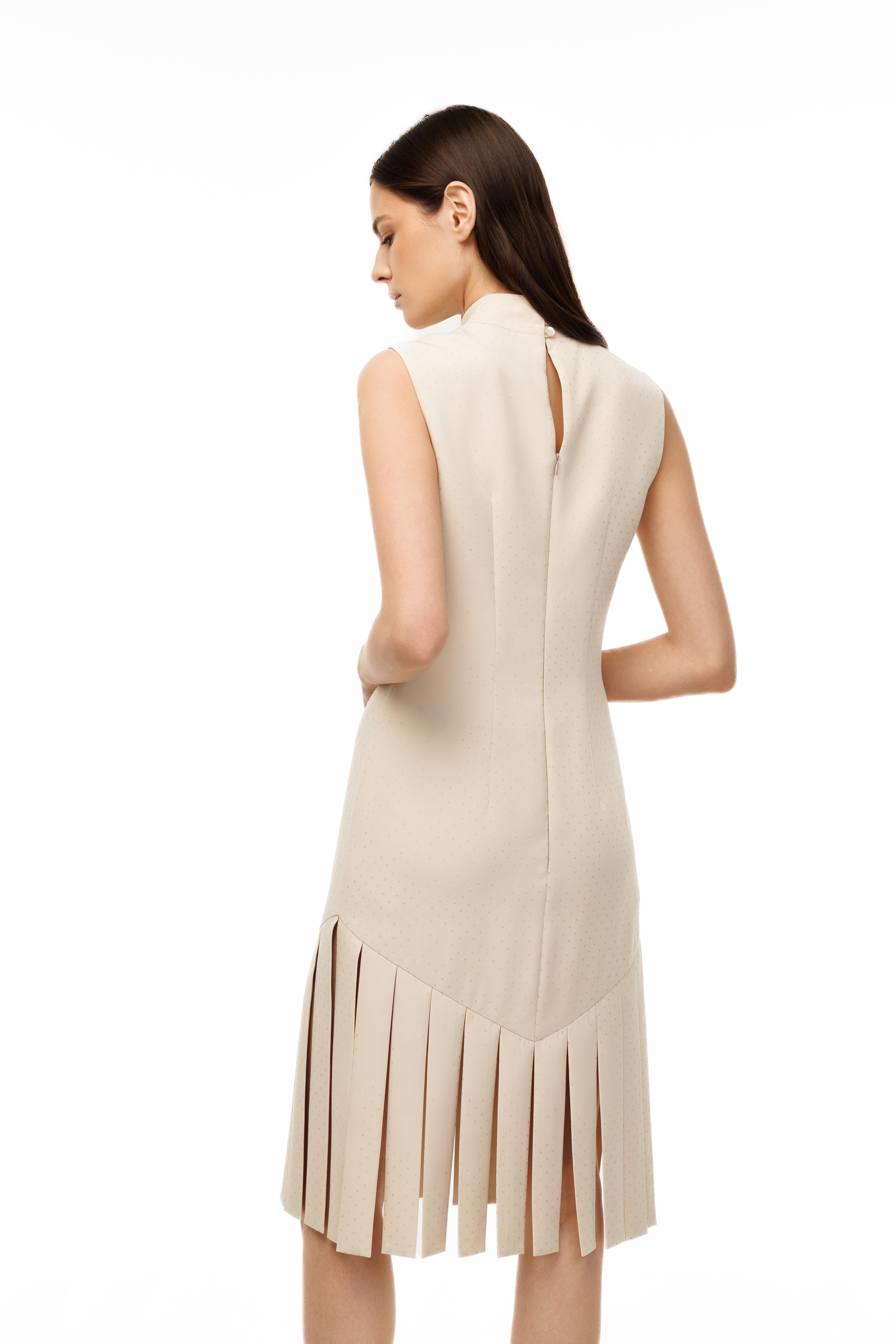 Woman wearing a beige sleeveless dress with pleated skirt on a white background