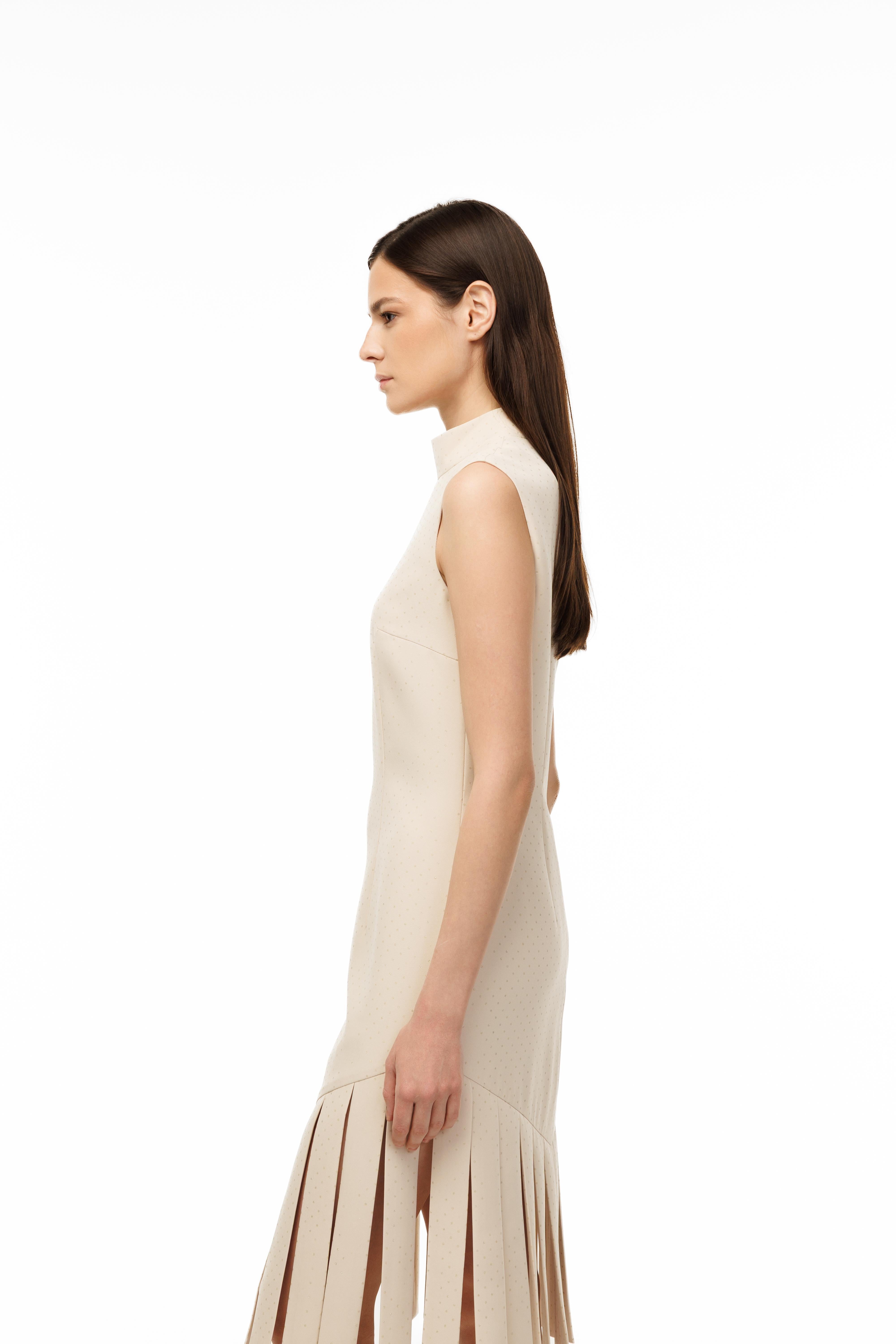 Woman wearing a beige sleeveless dress with fringe details on a white background