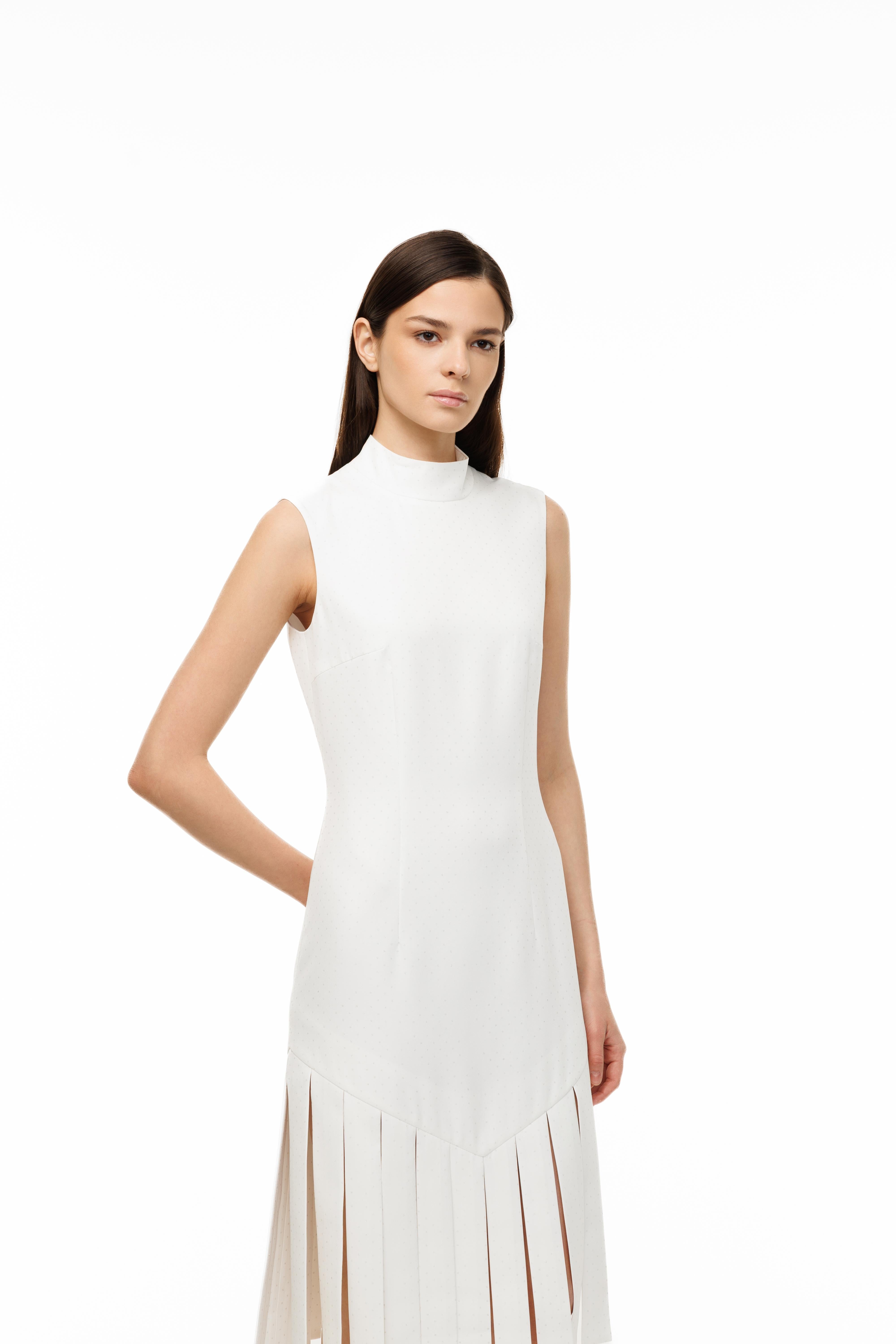 Woman wearing a white sleeveless dress with a high neckline and fringe details on a white background