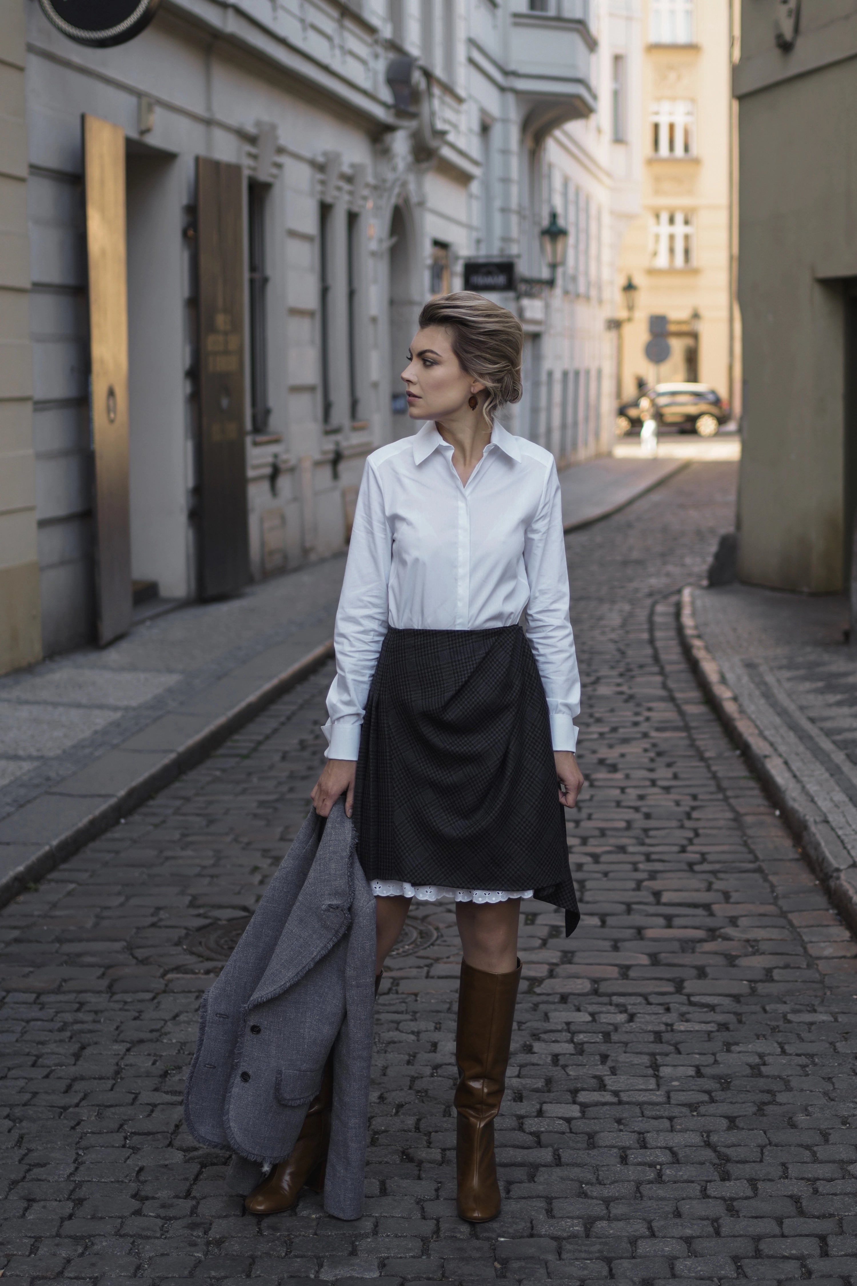Woman wearing Cotton shirt “Discret” in white from Mimaussy Paris, white shirt with black skirt standing on cobblestone street outdoors