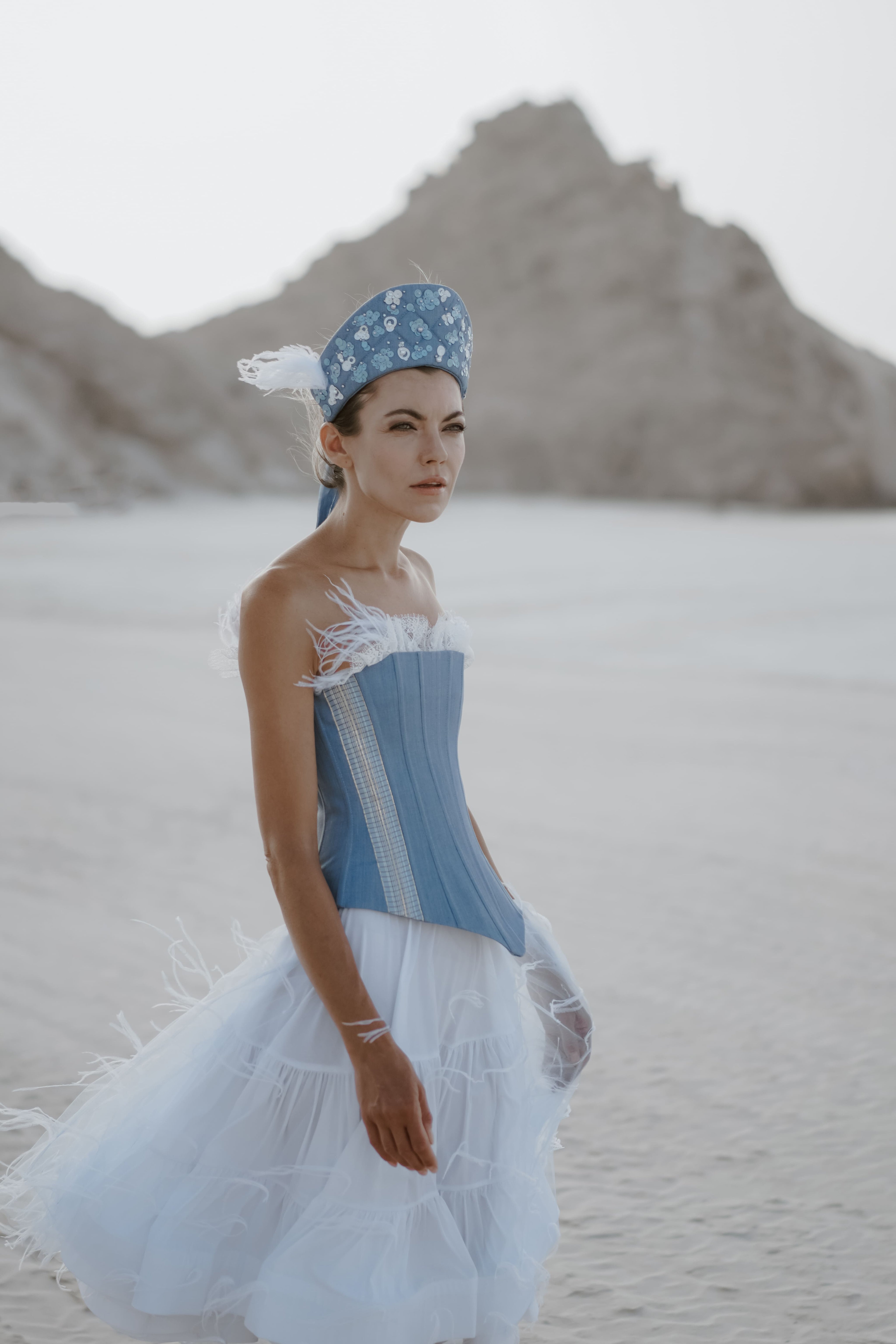 Woman in a blue and white corset dress with a headscarf standing in a desert landscape.