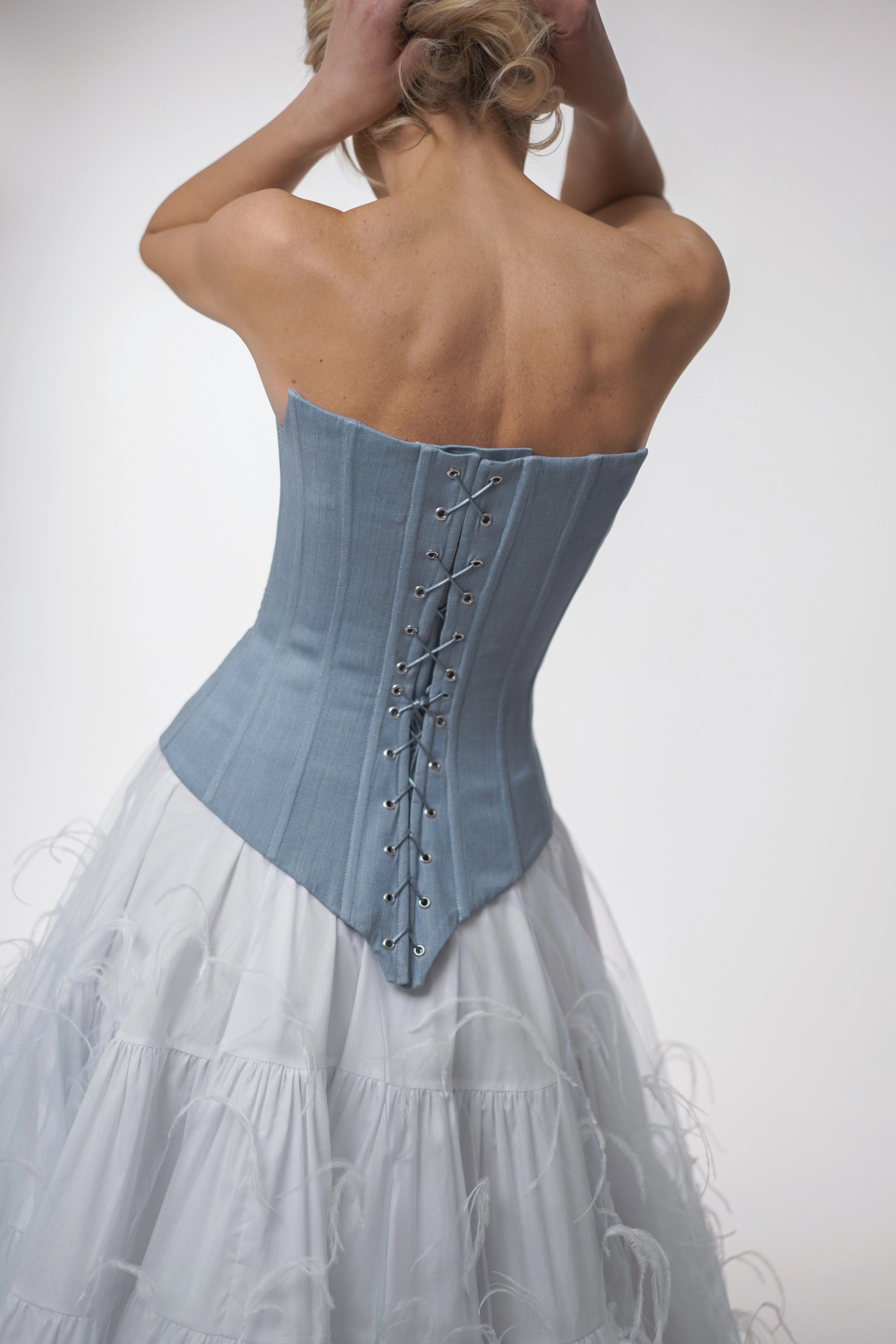 Woman wearing a blue corset and white skirt against a plain background