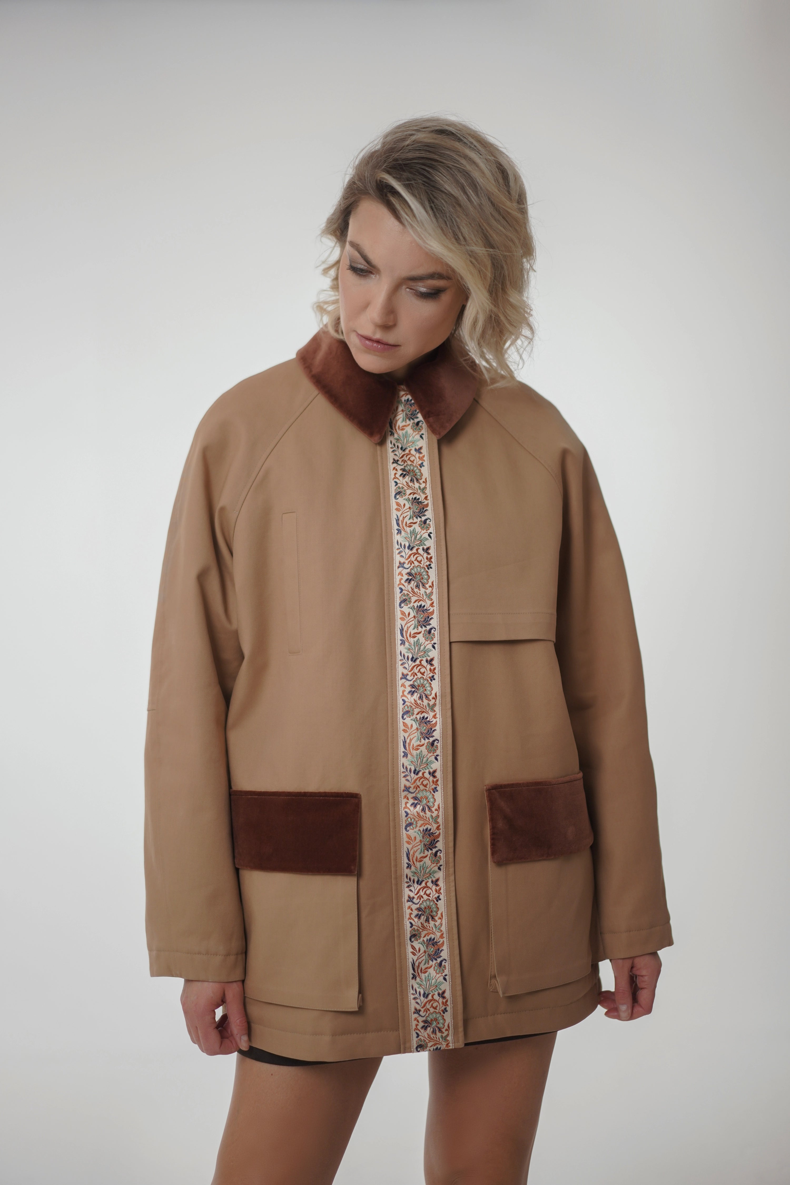 Woman wearing a brown coat with floral patterned lining on a white background