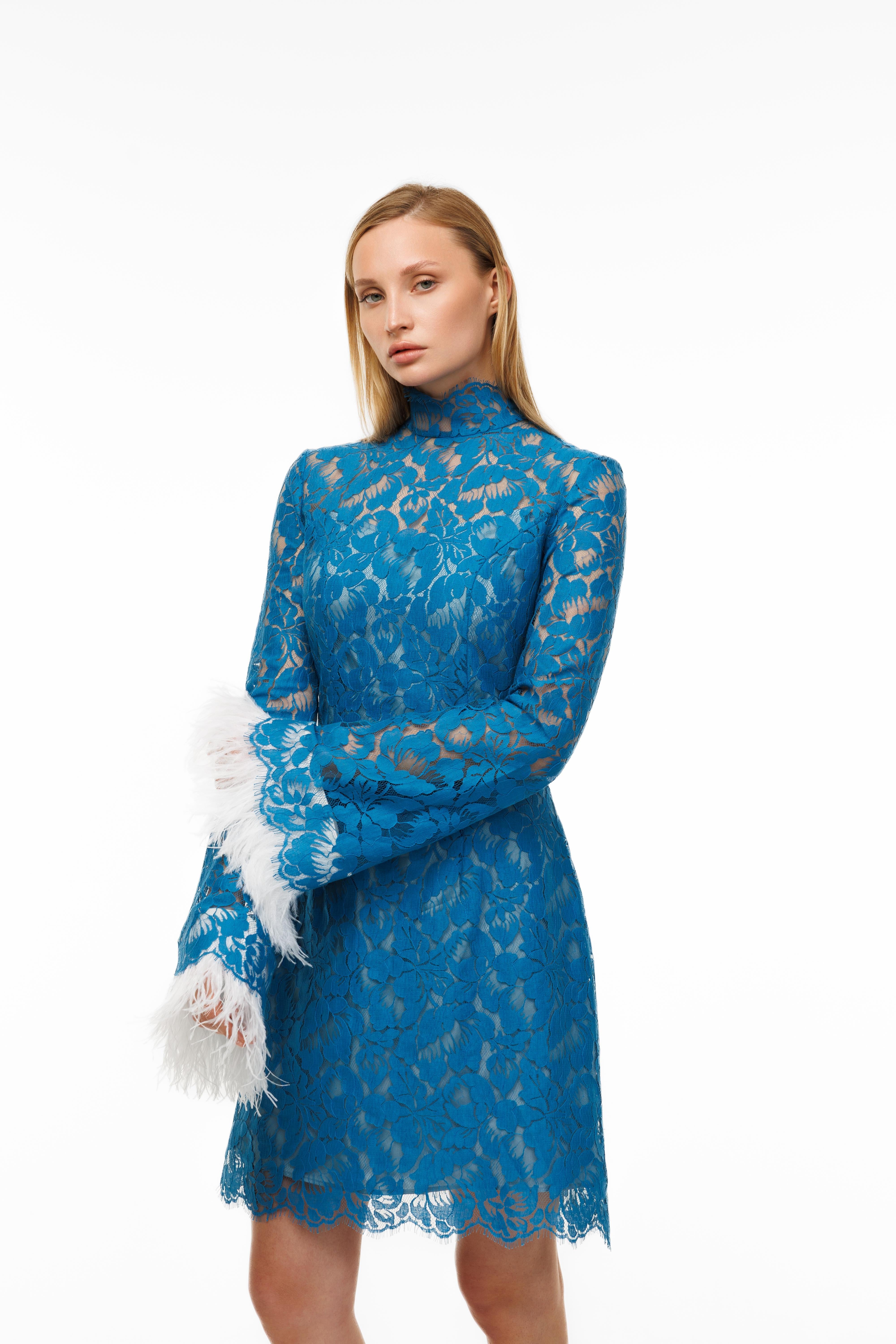 Woman wearing a blue lace dress with white feathered cuffs on a white background