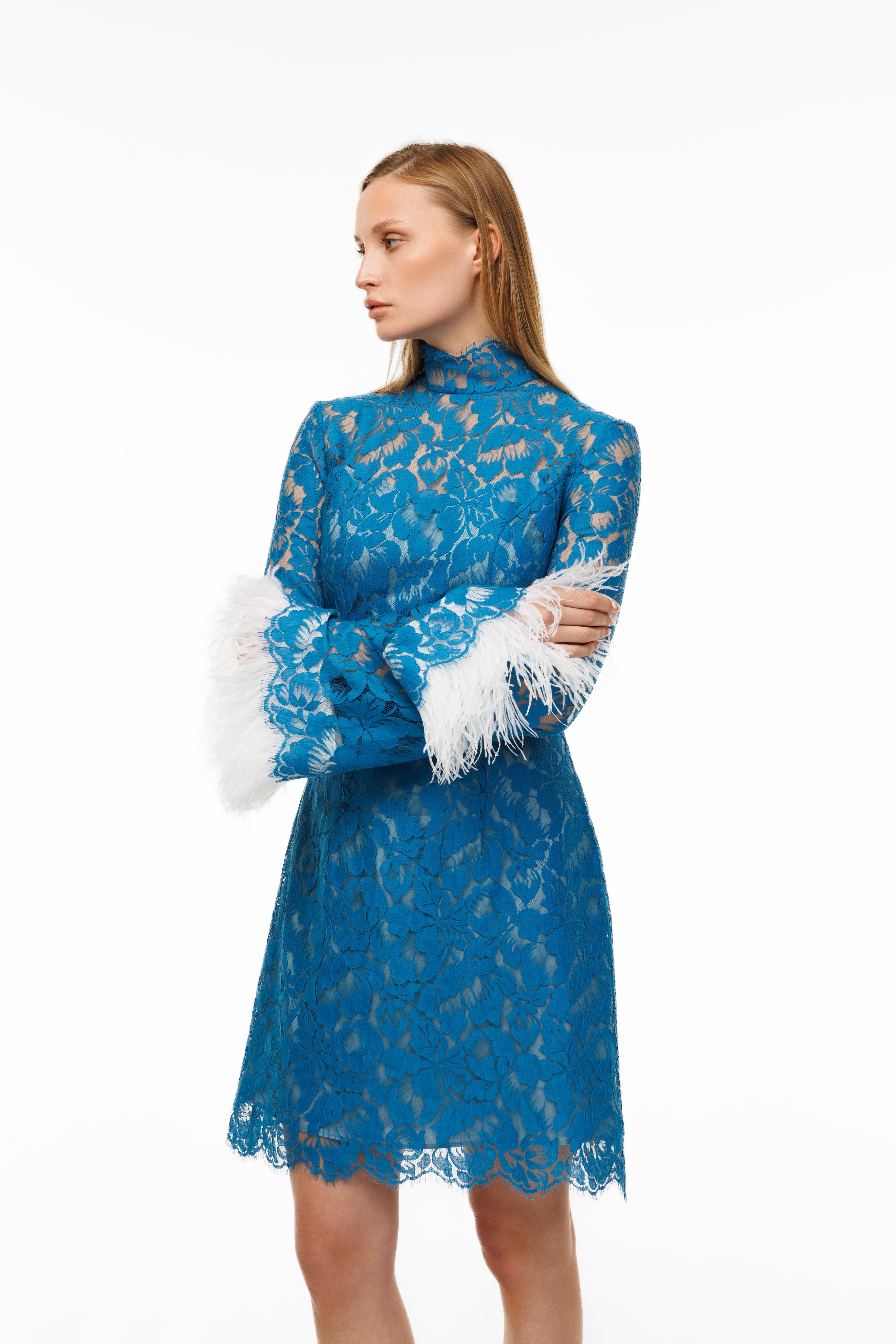 Woman wearing a blue lace dress with white cuffs and hem on a white background