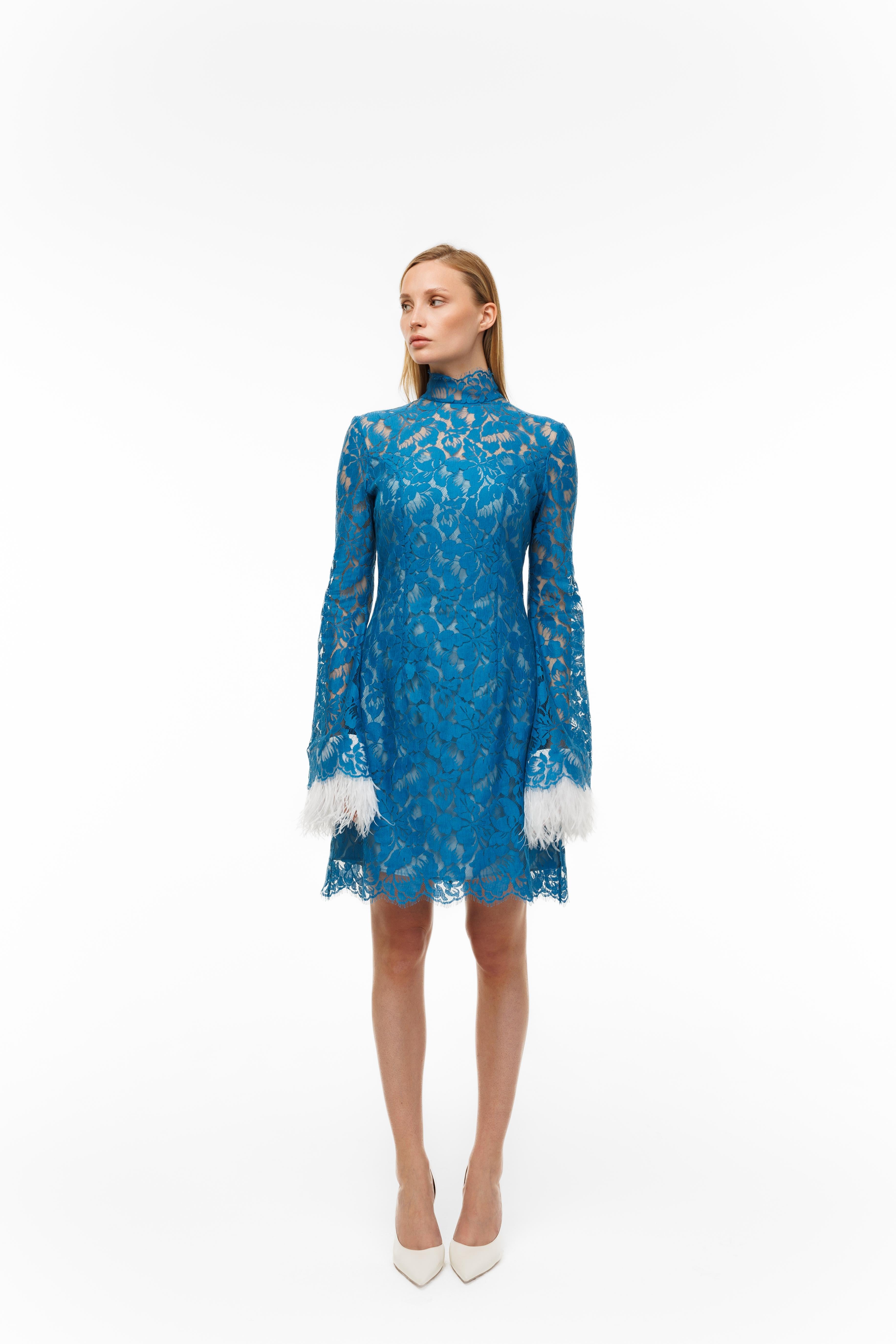 Woman wearing a blue lace dress with white cuffs and hem on a white background