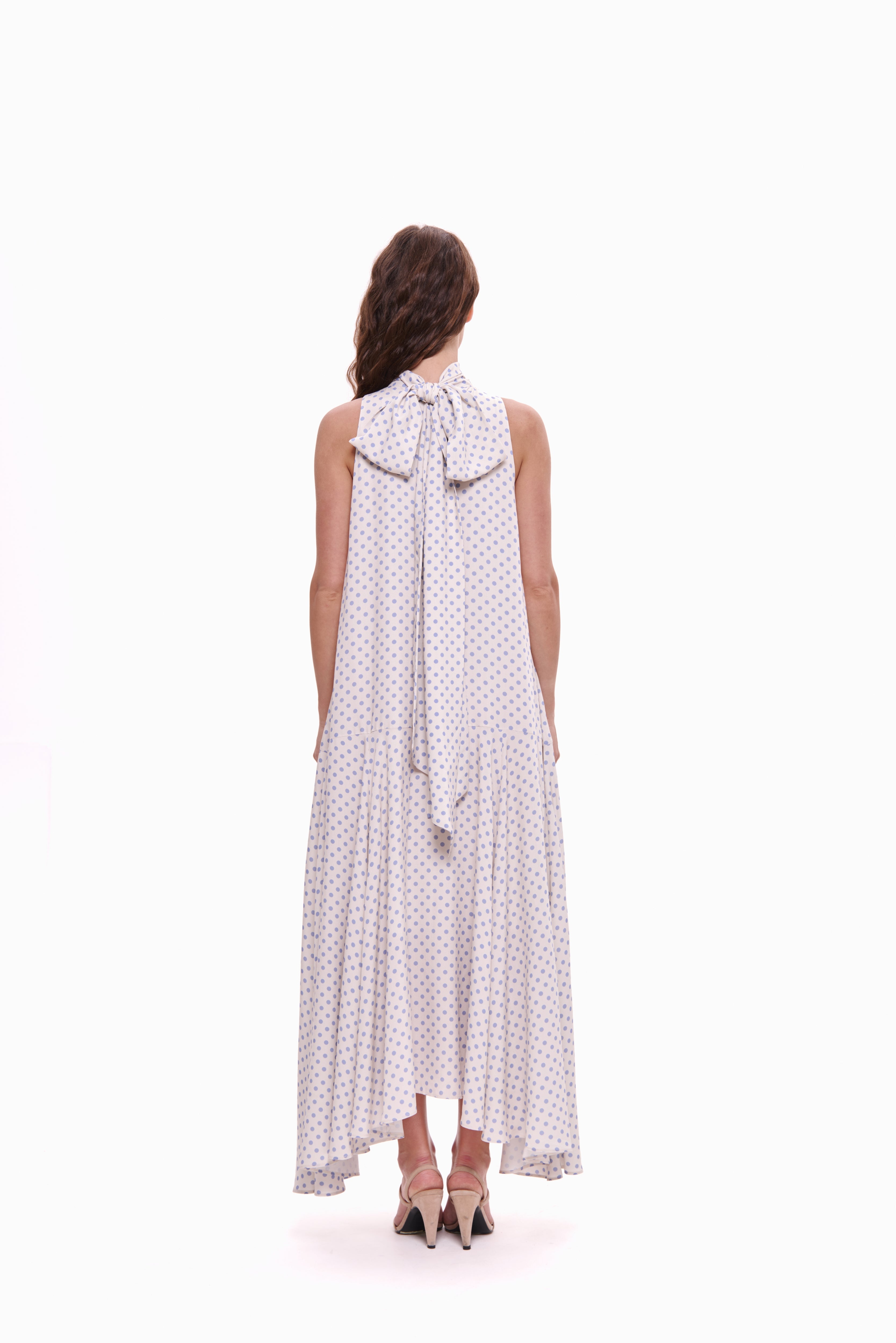 Woman wearing a white polka dot dress with a bow detail on a white background
