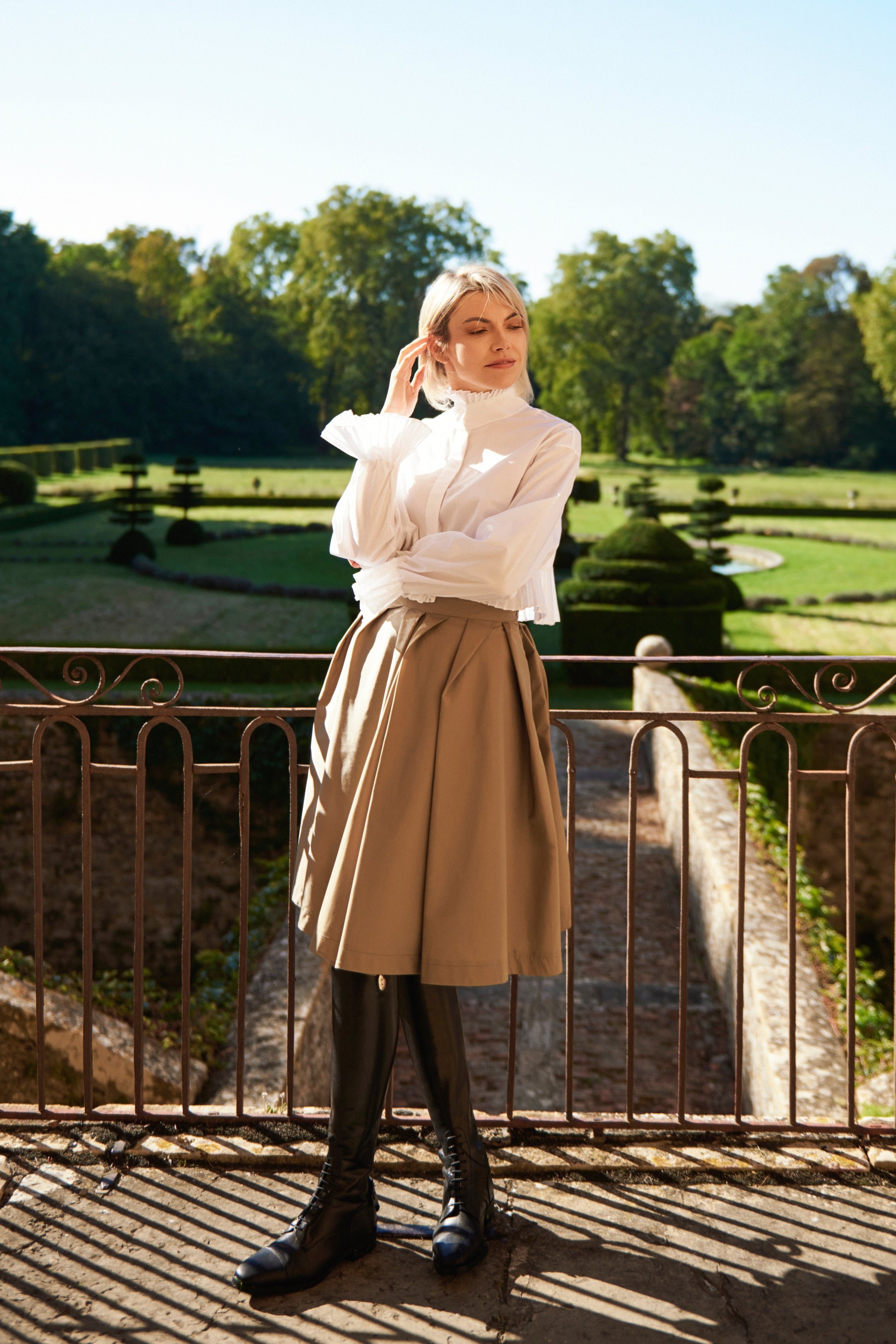 Woman wearing a Mademoiselle Plissé cropped shirt-blouse from Mimaussy Paris, beige skirt, in a park with trees and clear sky