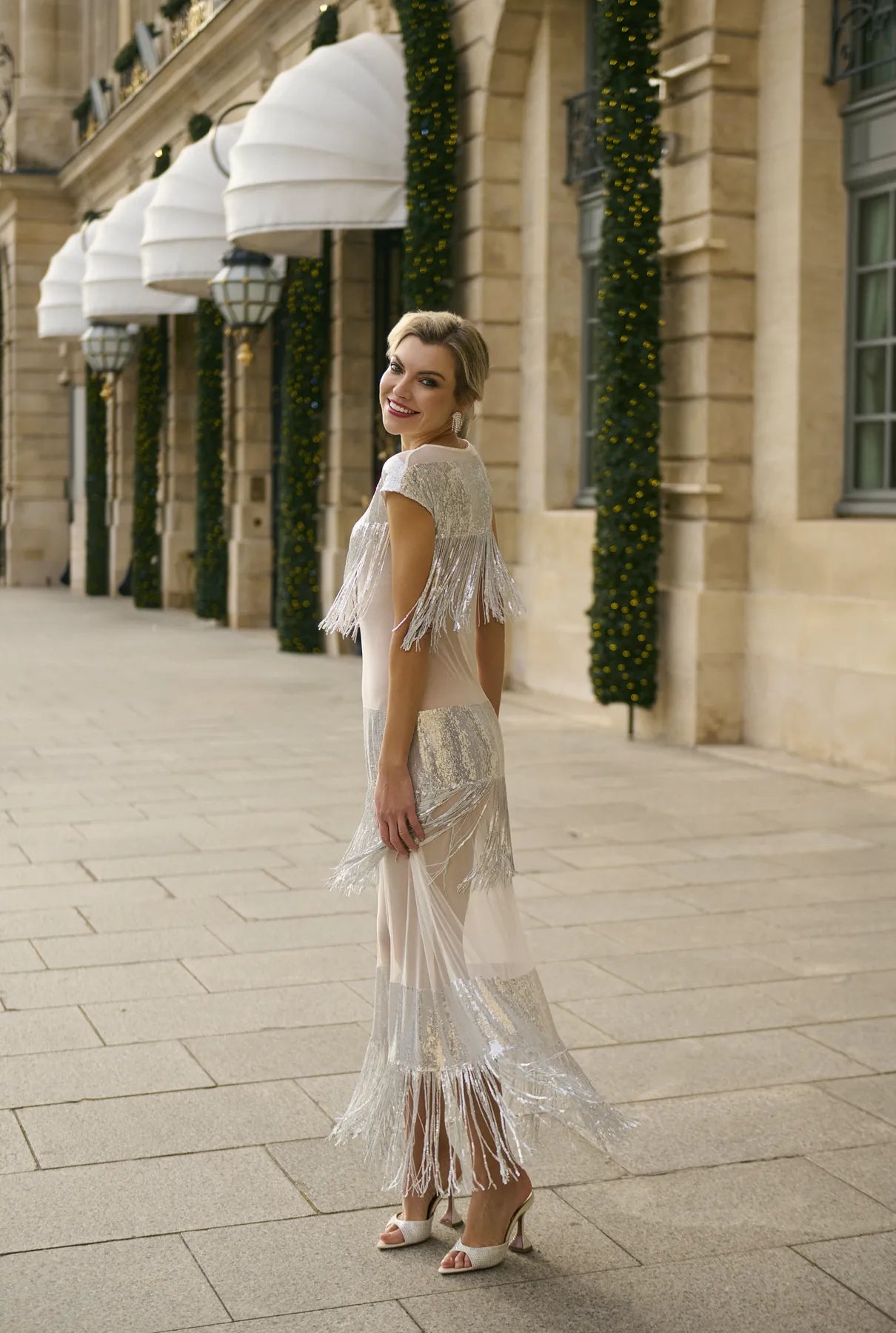 A woman in a silver Midnight Charleston Dress by Mimaussy Paris stands elegantly on a sidewalk.