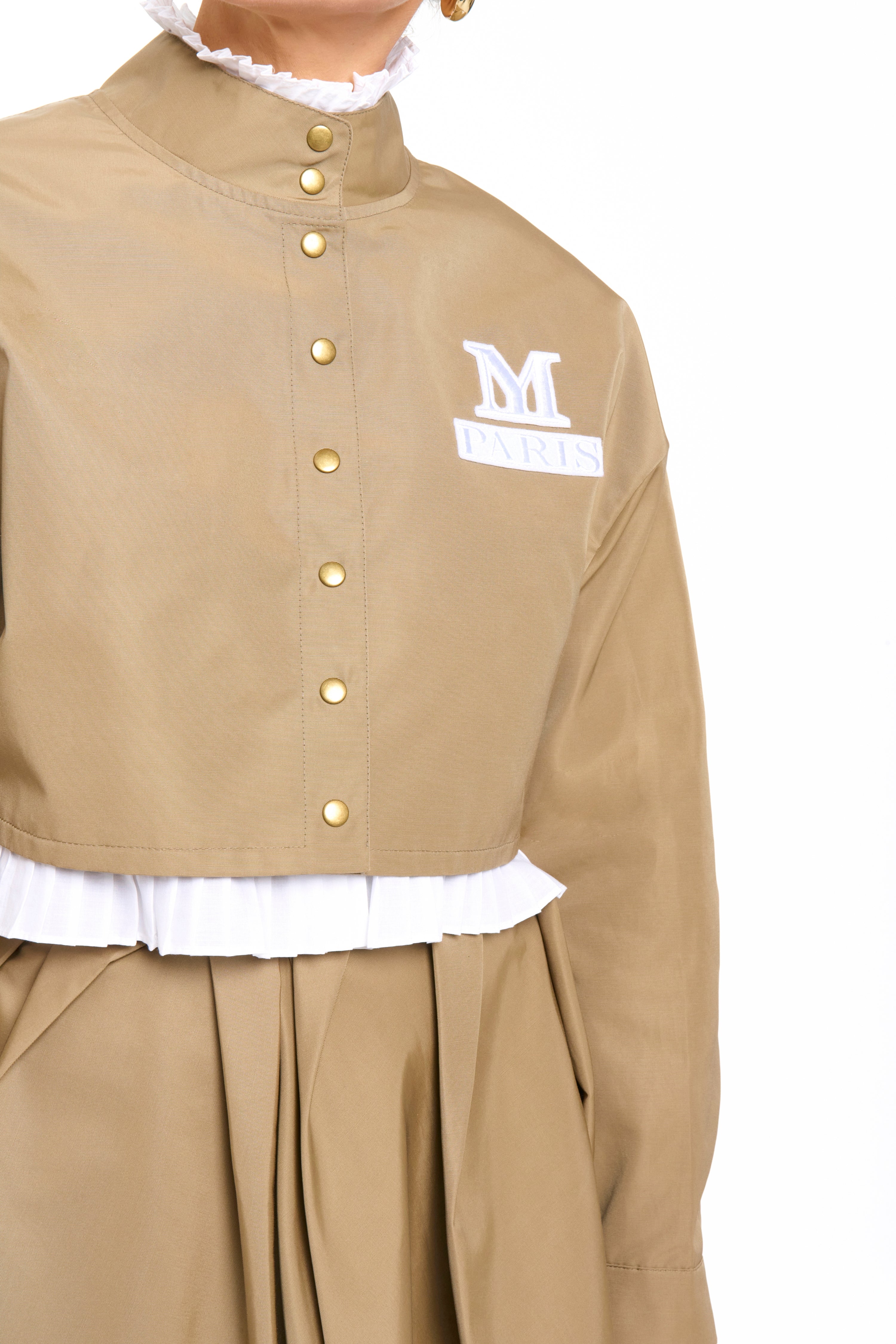 Woman wearing a Parisien Cropped Trench Jacket from Mimaussy Paris, beige jacket with logo on the chest, on a white background