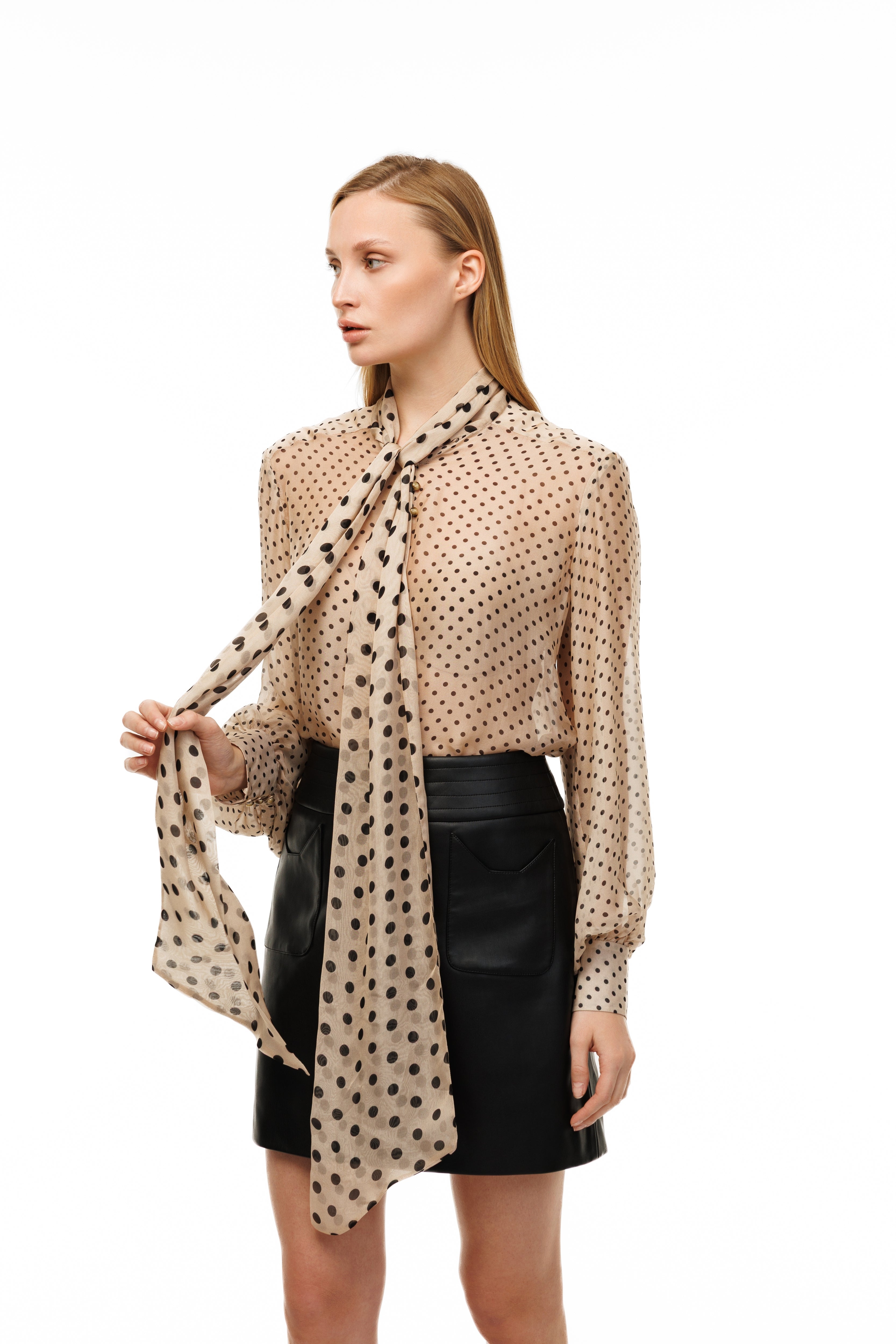 Woman wearing a beige polka dot blouse and black skirt with a matching scarf on a white background