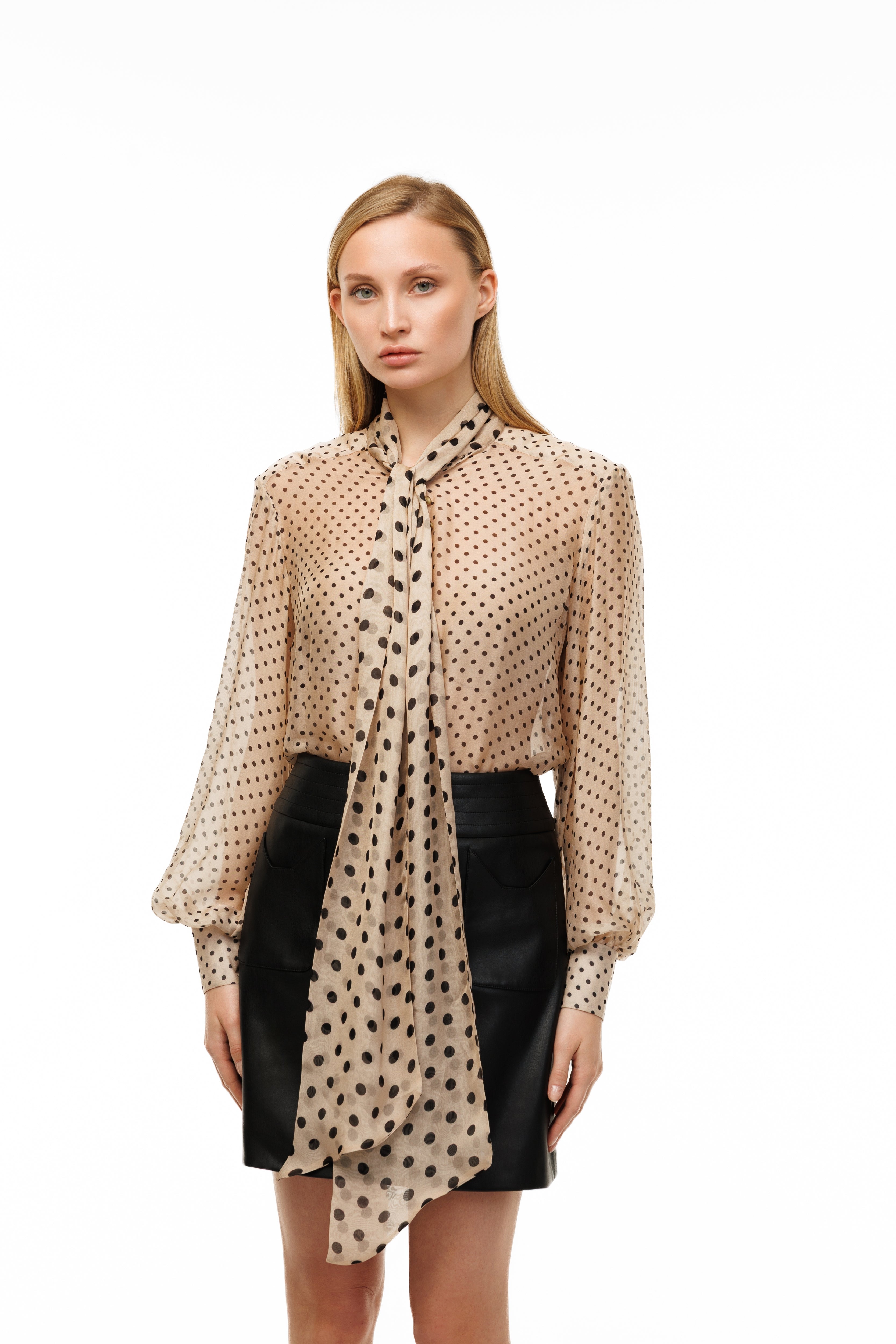 Woman wearing a beige polka dot blouse with a black skirt on a white background