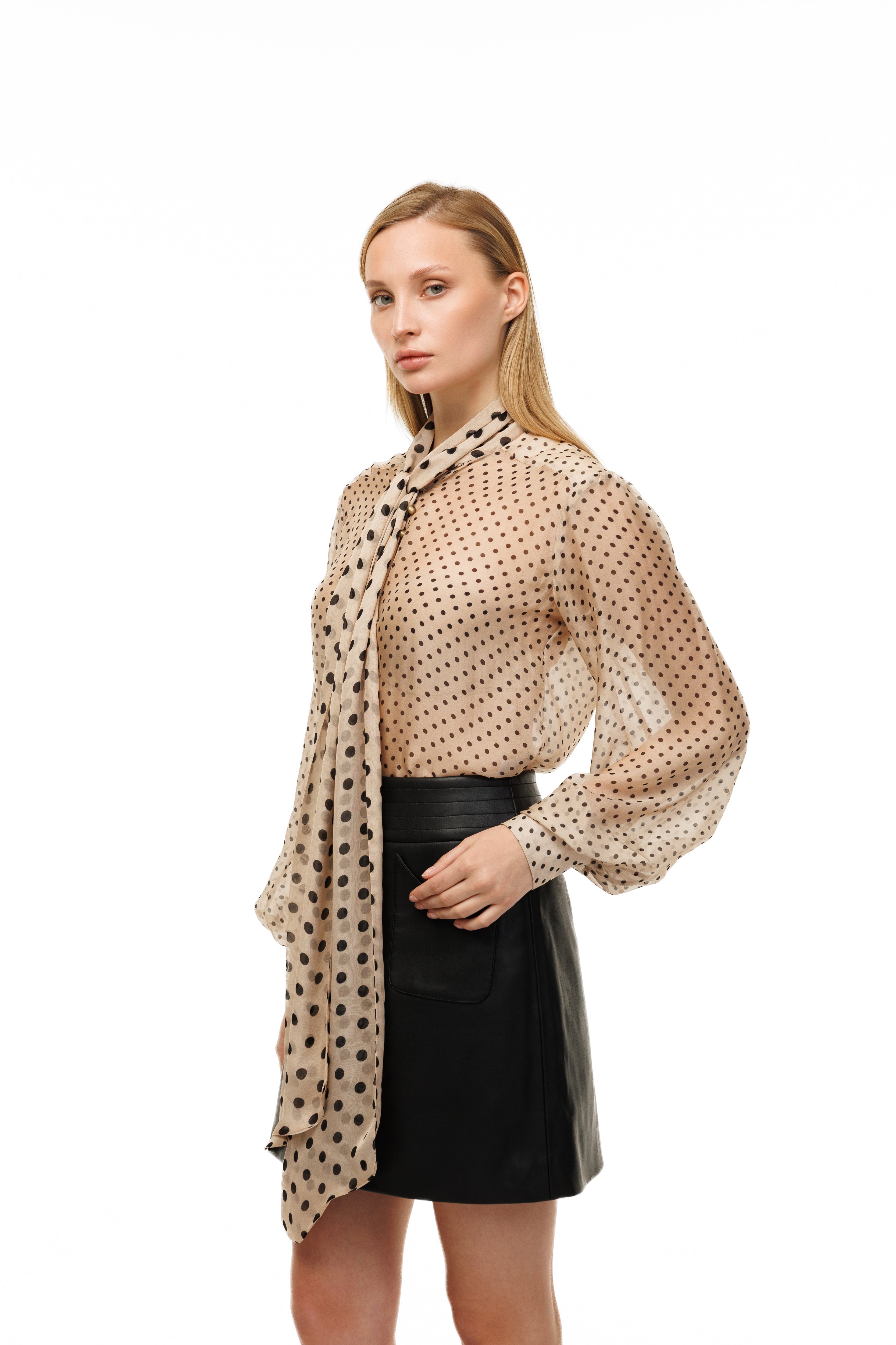 Woman wearing a beige polka dot blouse and black skirt with a patterned scarf on a white background