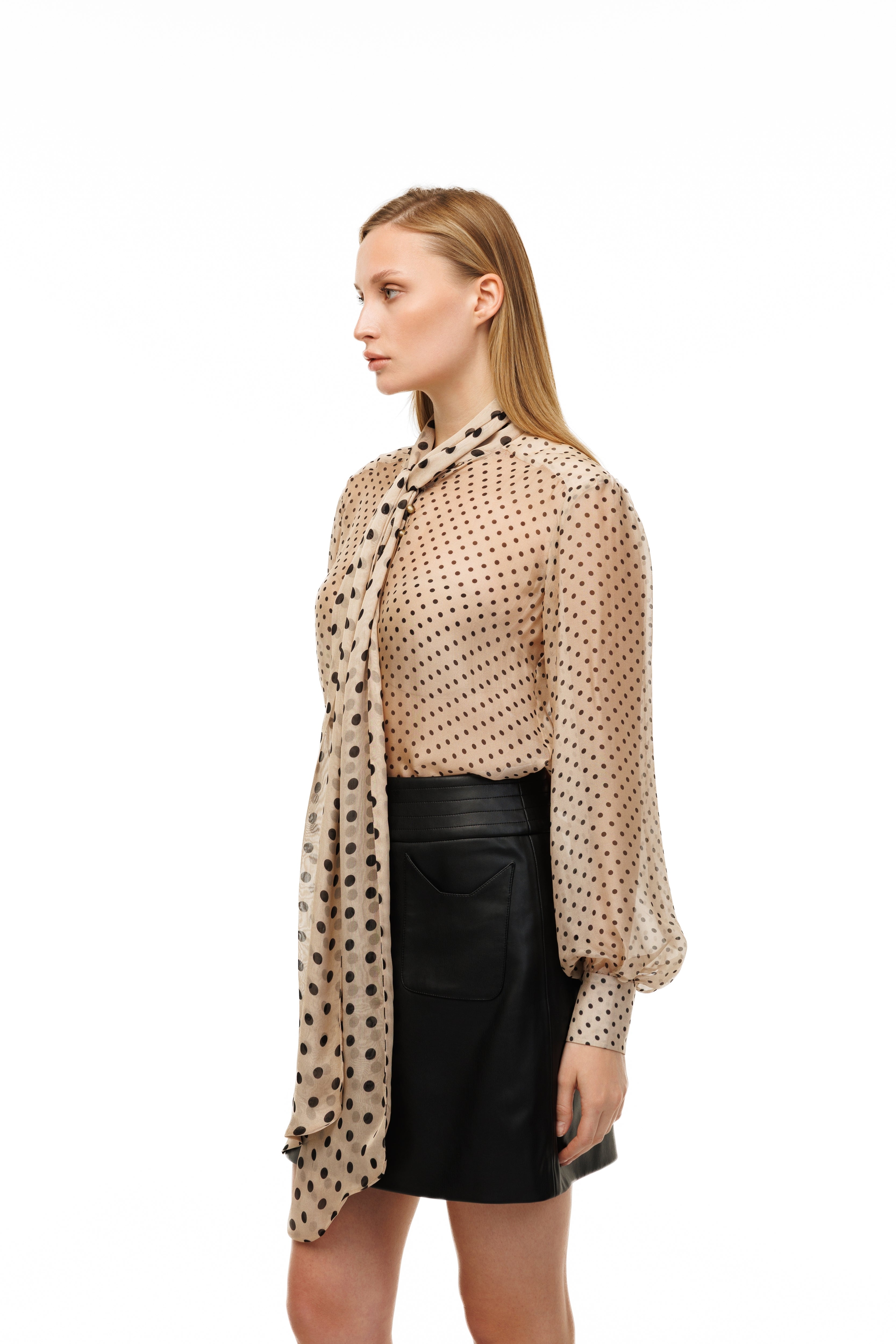 Woman wearing a beige polka dot blouse and black skirt with a patterned scarf on a white background