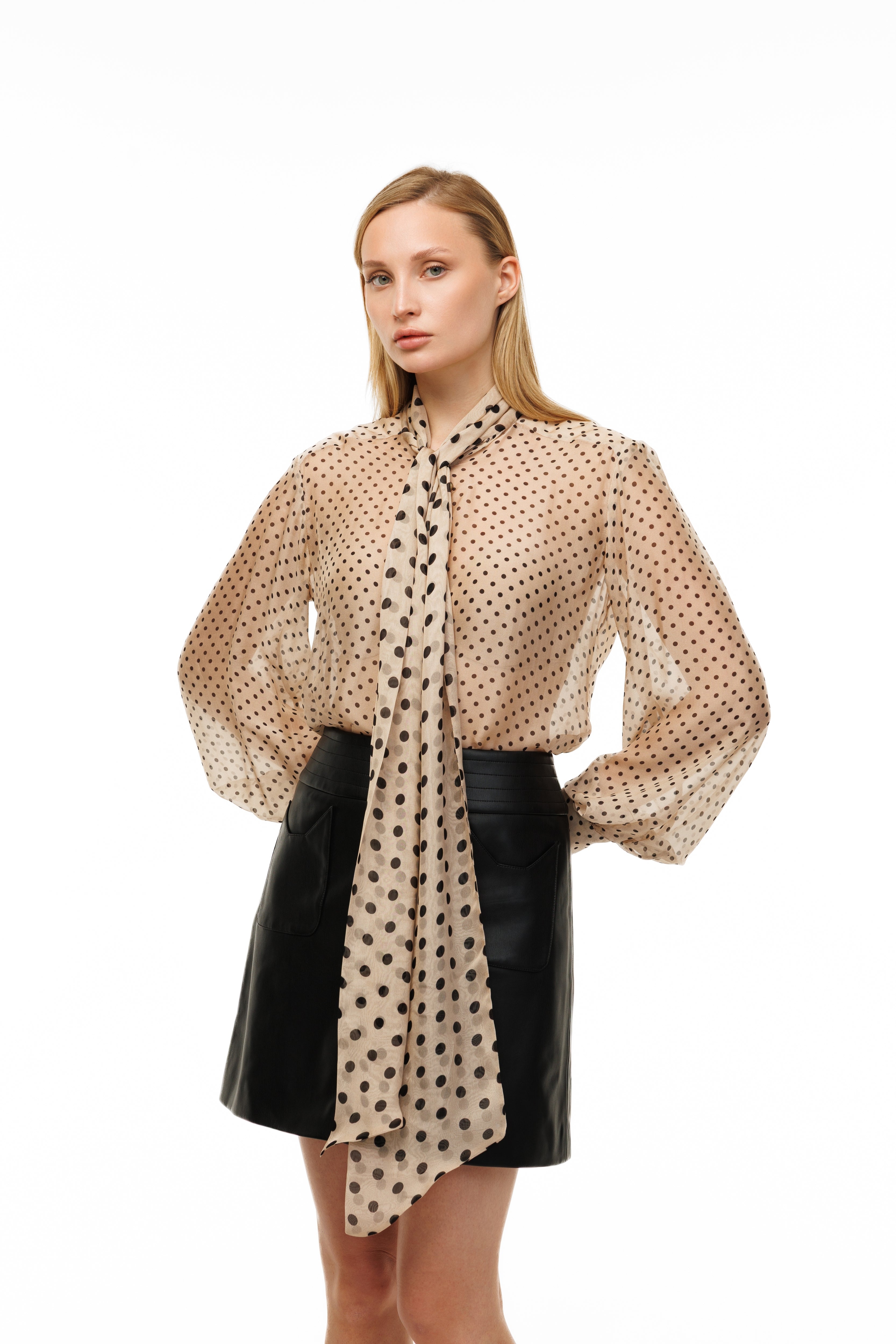 Woman wearing a beige polka dot blouse with a black leather skirt on a white background