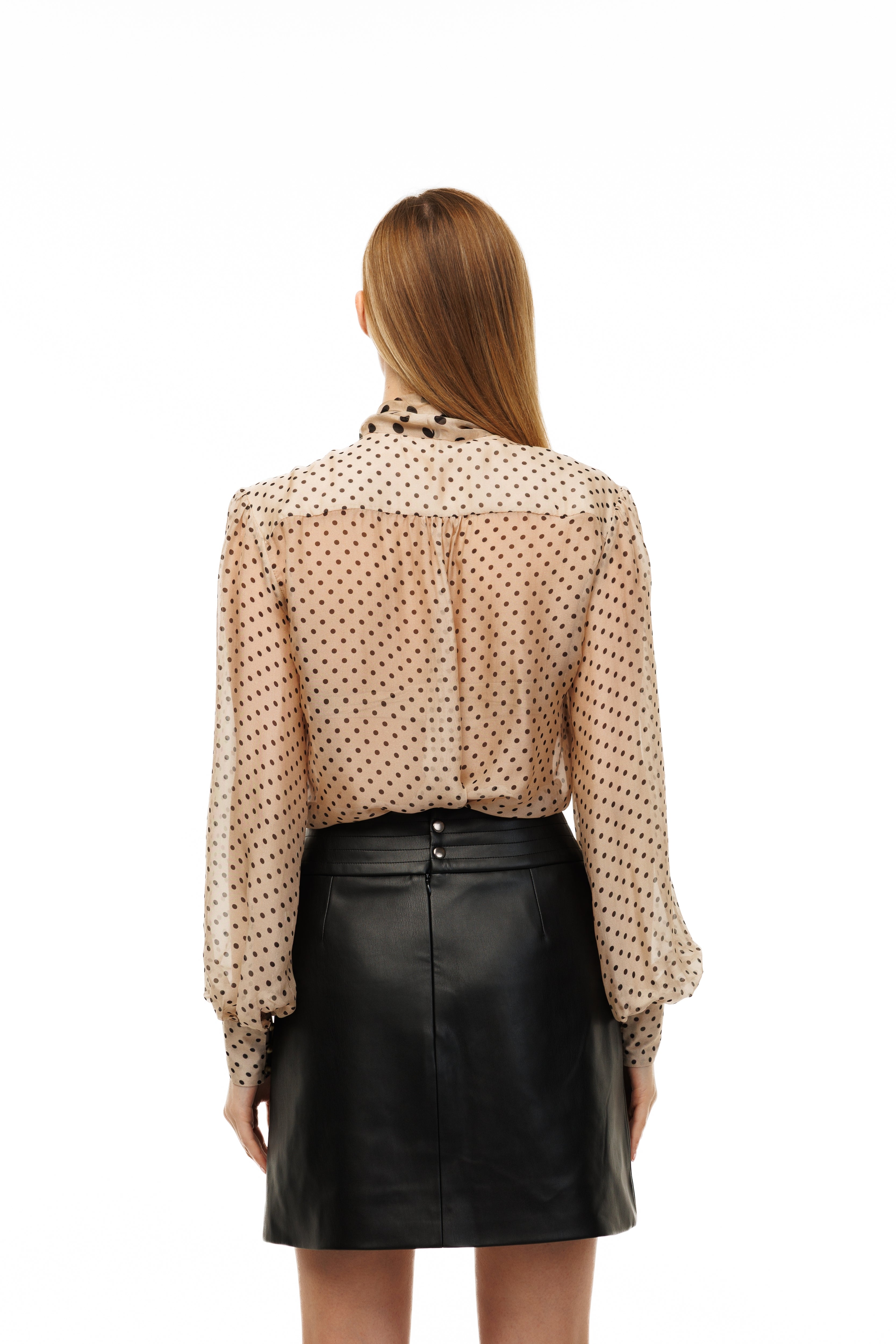 Woman wearing a polka dot blouse and black leather skirt on a white background