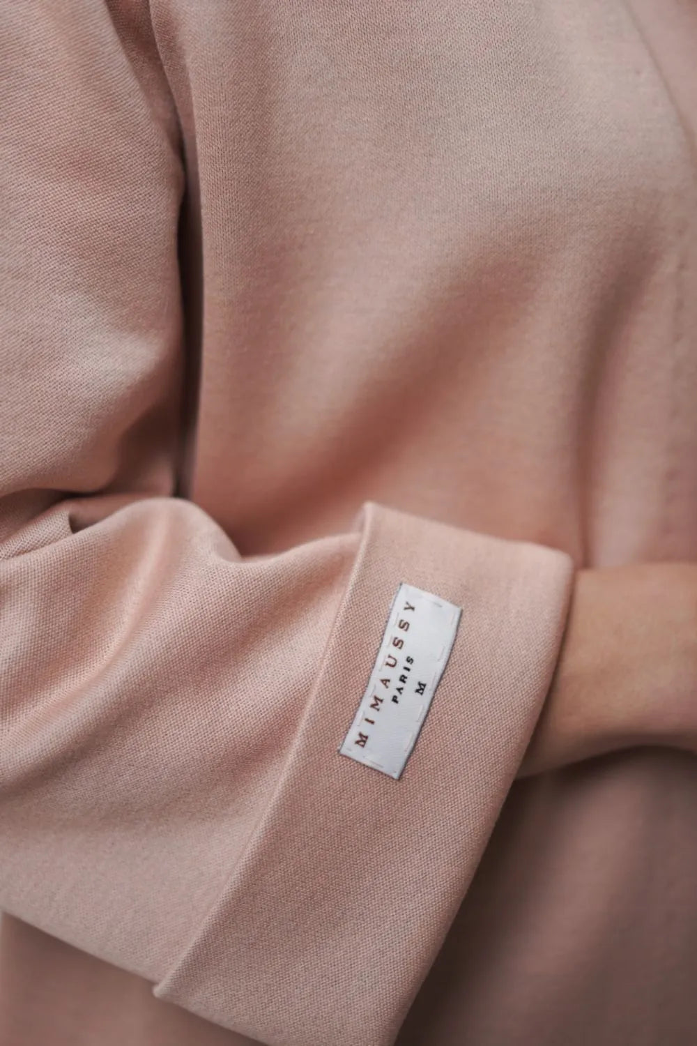 Close-up of a pink Mimaussy Paris robe coat with ostrich feathers and a label on the sleeve.