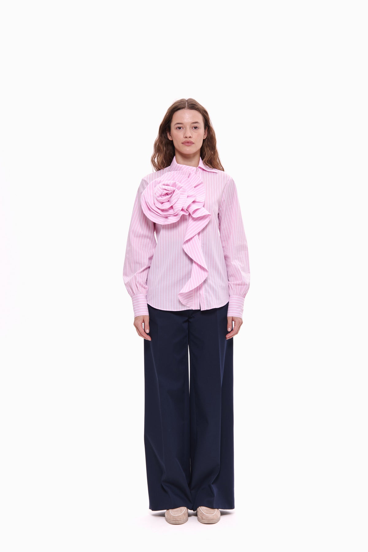 Woman wearing a pink blouse with a large floral design and dark pants on a white background