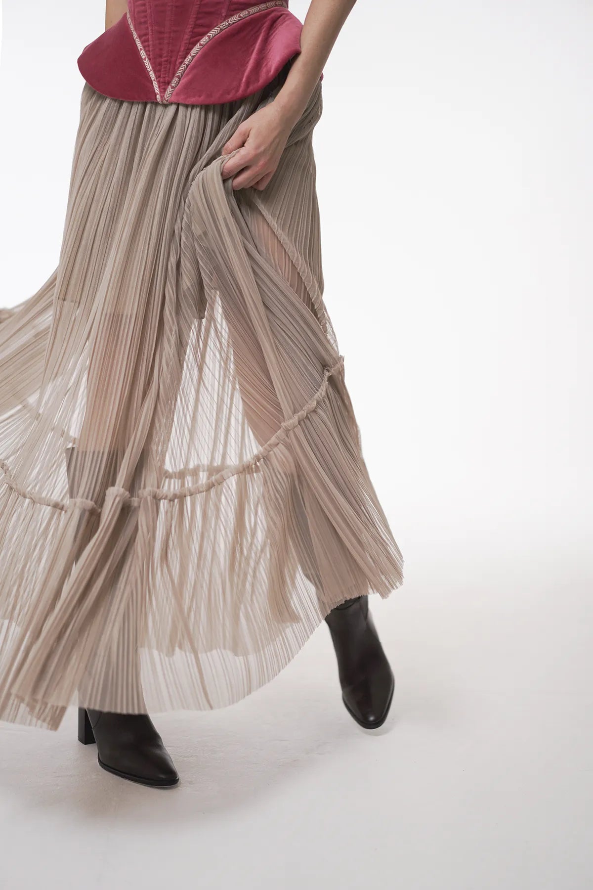 A woman in a fashionable long skirt and boots, featuring the luxury Sauvage Plissee Skirt by Mimaussy Paris.