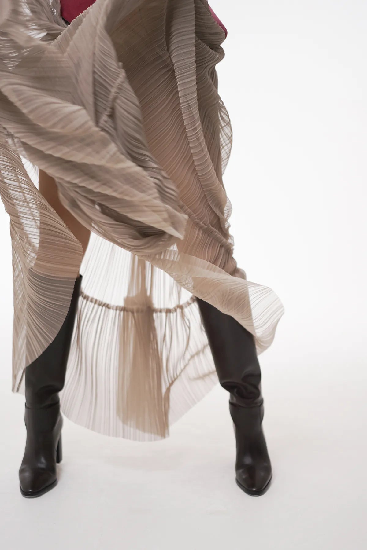 A woman in a skirt and boots, featuring the Sauvage Plissee Skirt from Mimaussy Paris, dances with elegance and energy.