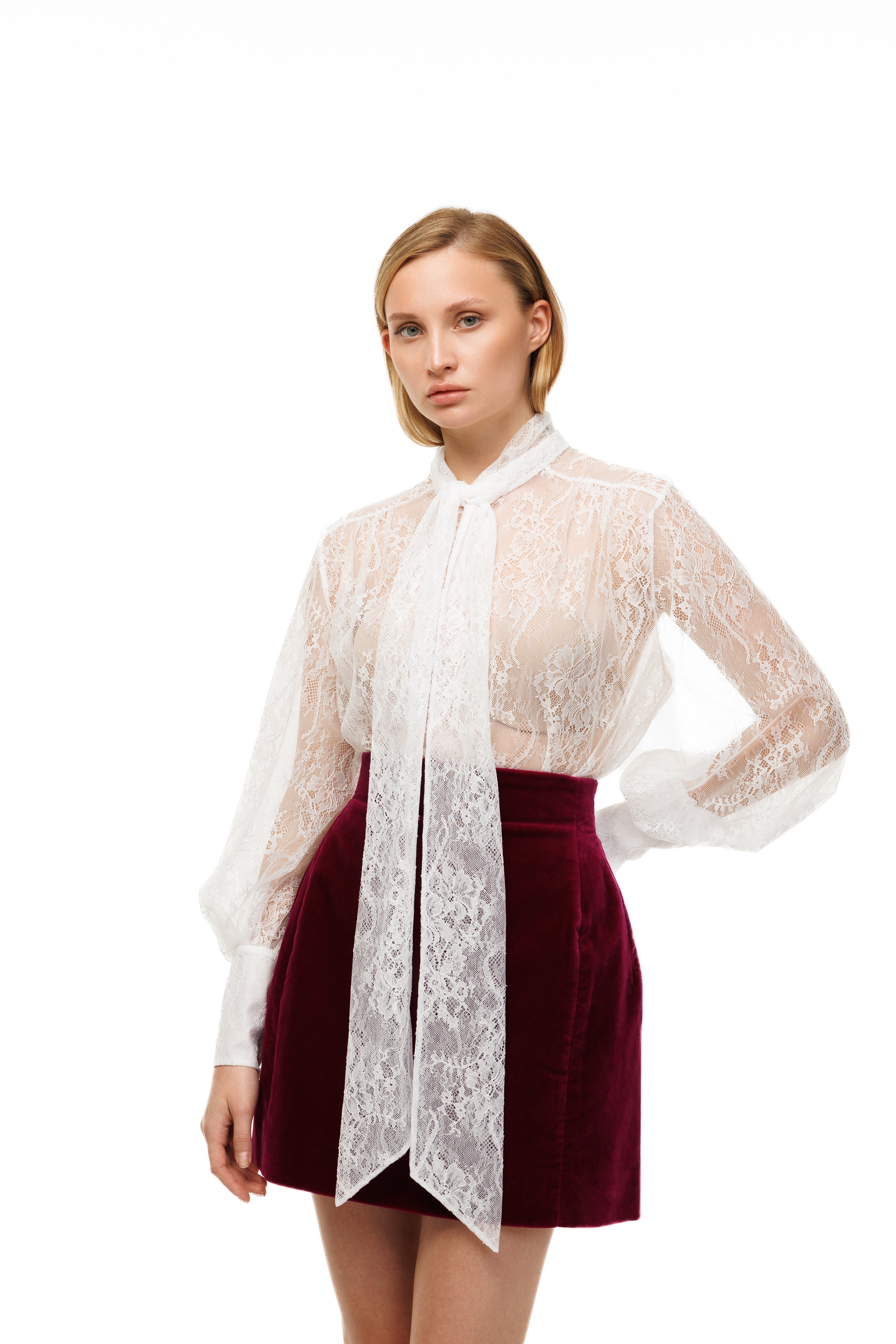 Woman wearing a white lace blouse and maroon skirt on a white background