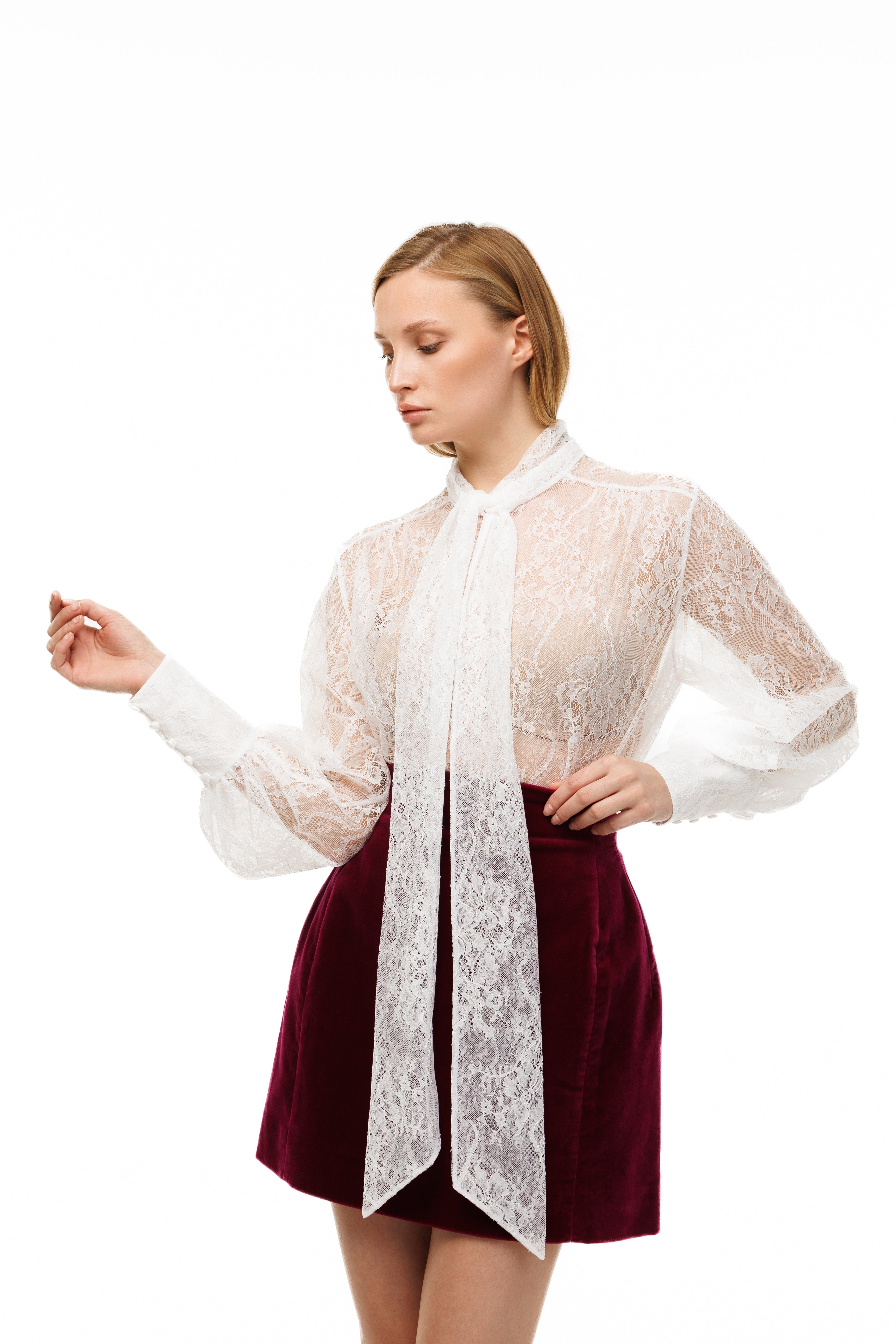 Woman wearing a white lace blouse over a burgundy skirt on a white background