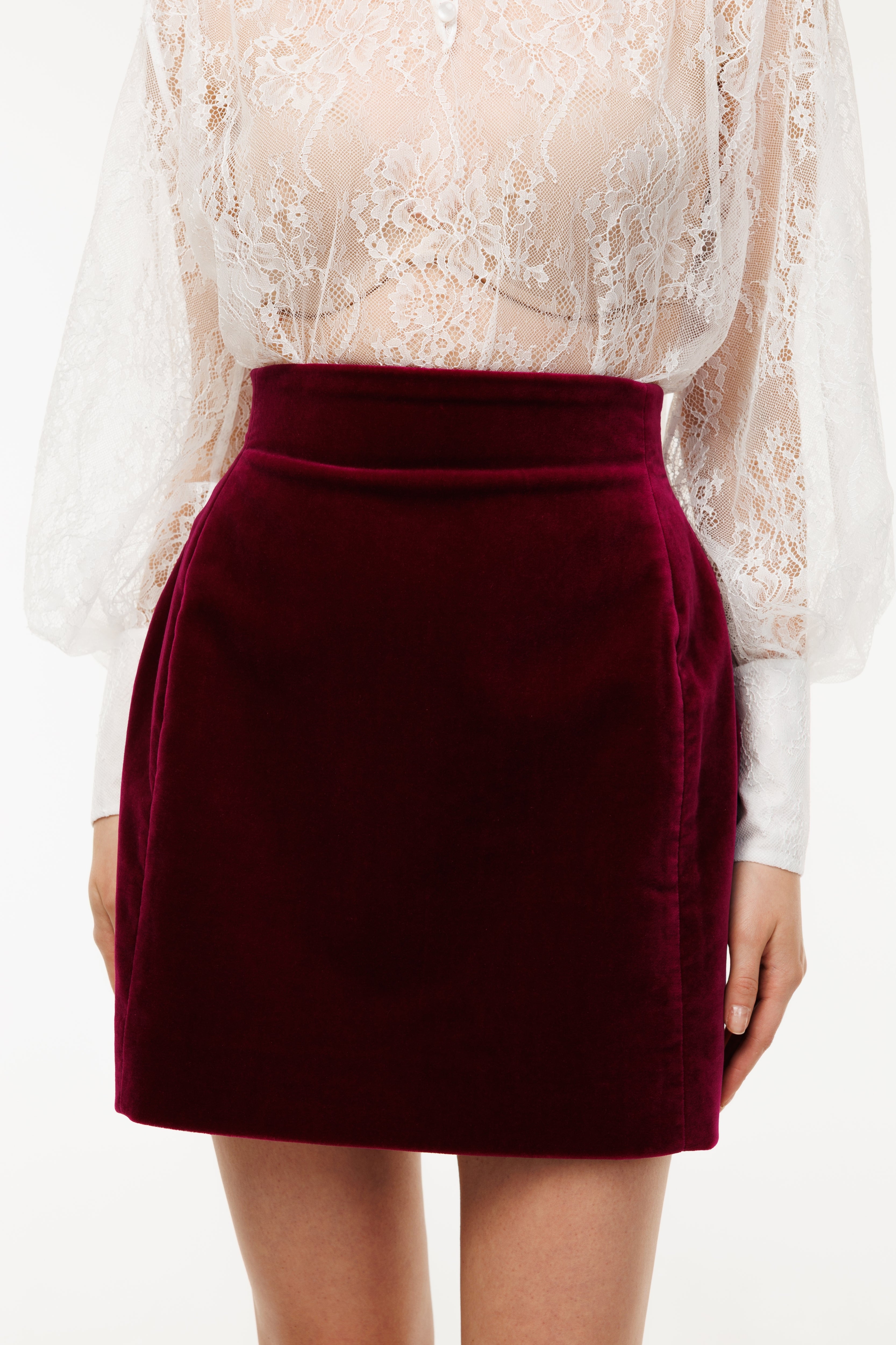 Maroon skirt worn with a white lace top on a plain background