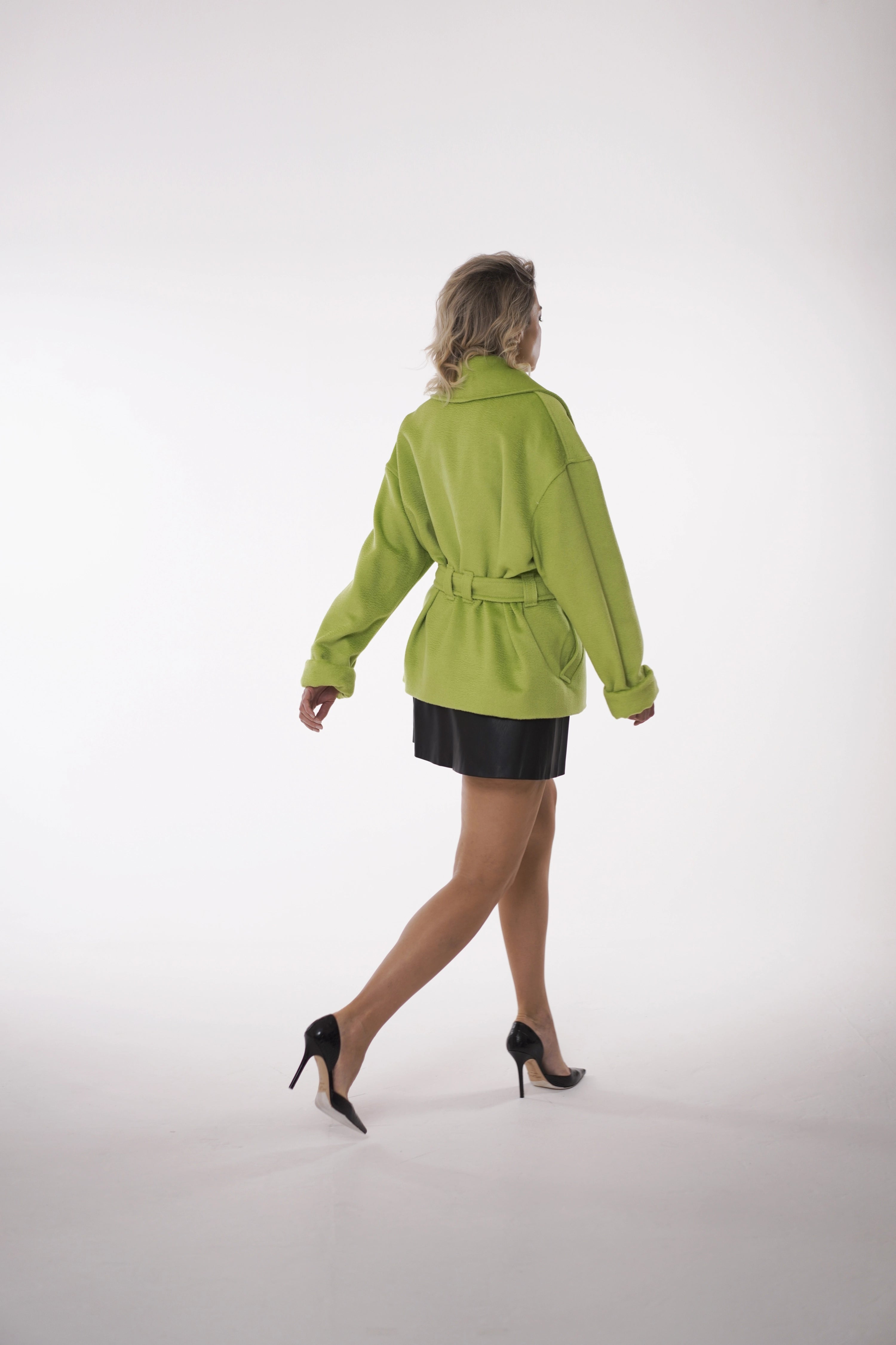Woman wearing Spring Touch Coat from Mimaussy Paris, angled back view of bright green coat with model walking on white background, studio setting