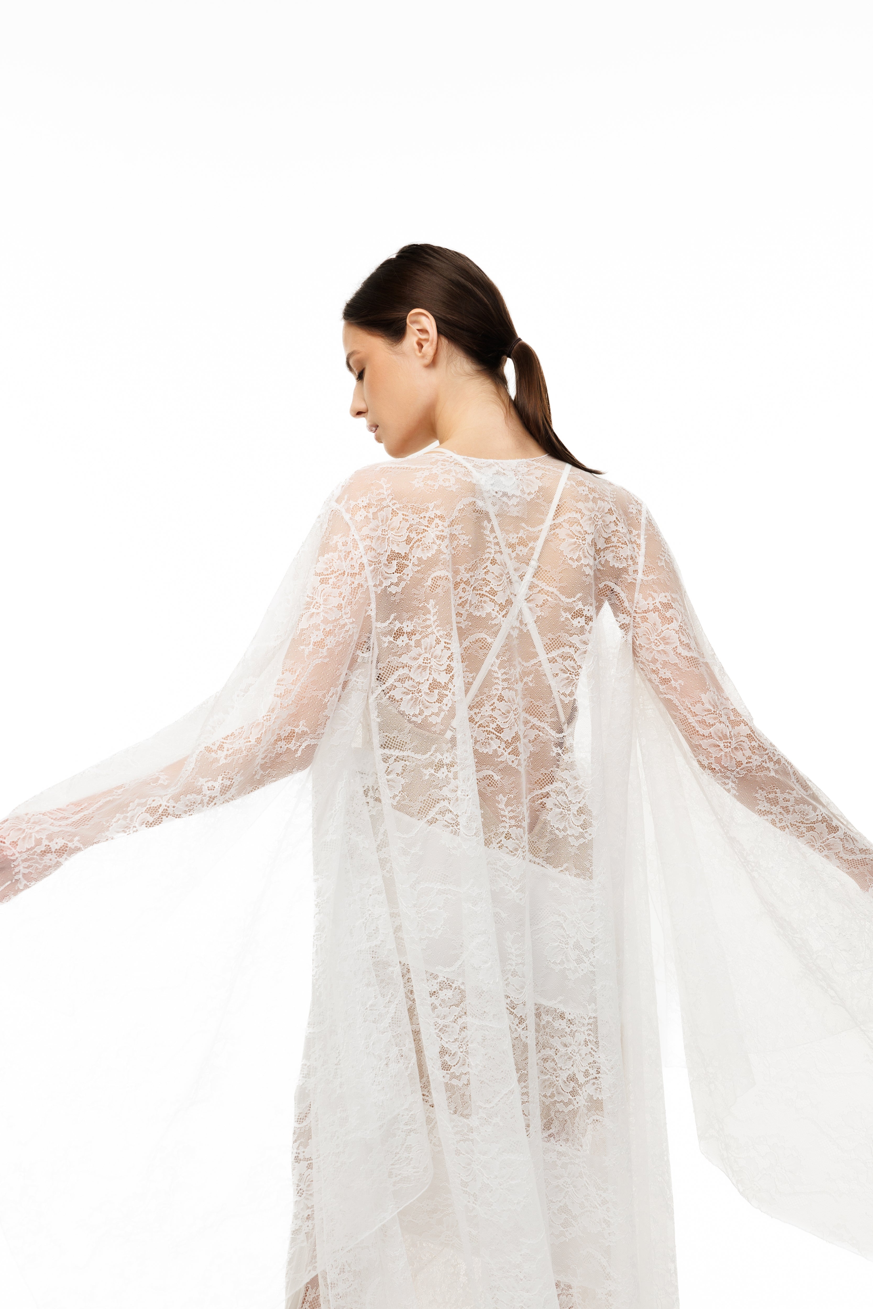 Woman wearing a sheer white lace dress on a white background
