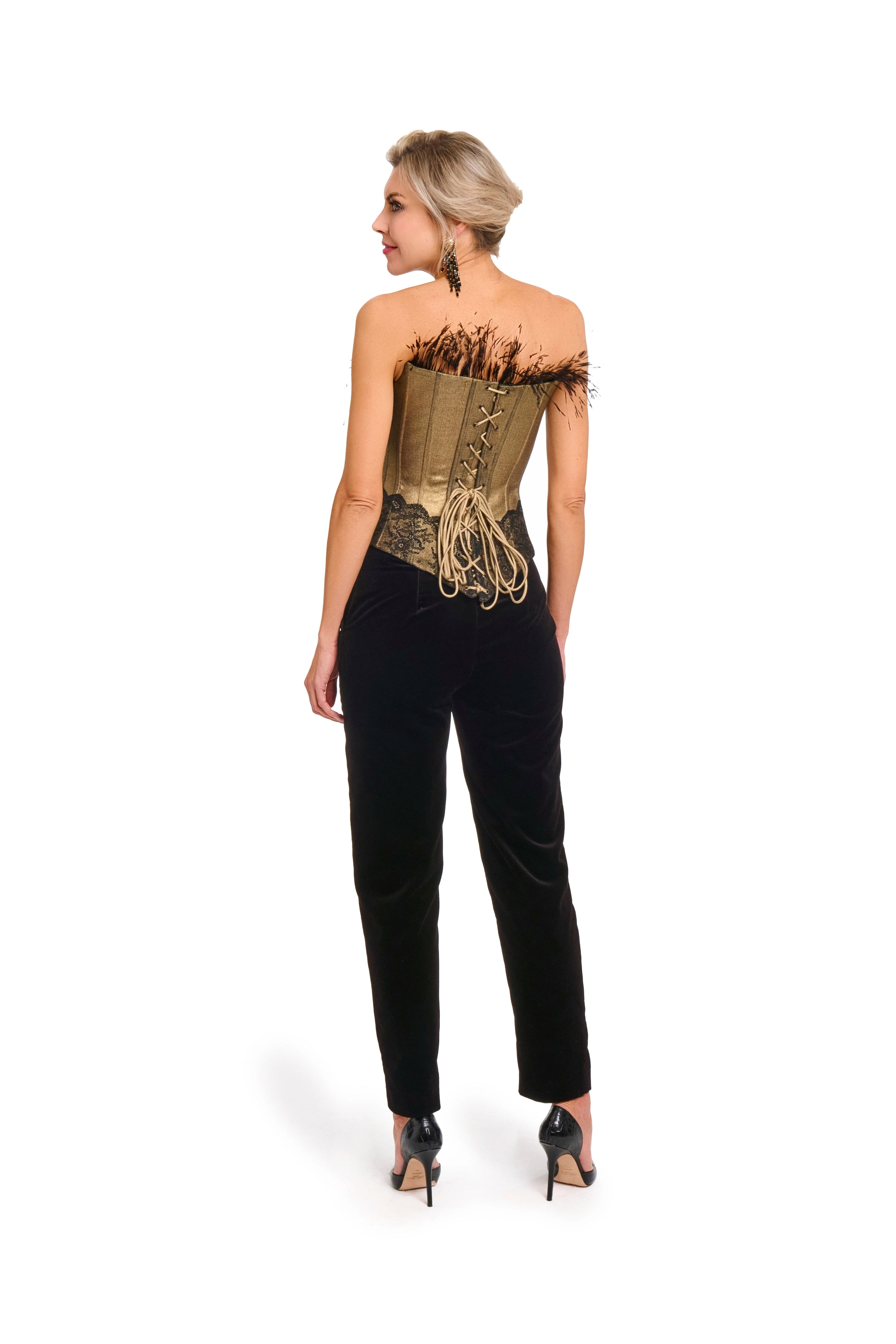Woman wearing Velvet trousers from Mimaussy Paris, full-length back view of black velvet pants with gold strapless top with feather details on white background, studio setting
