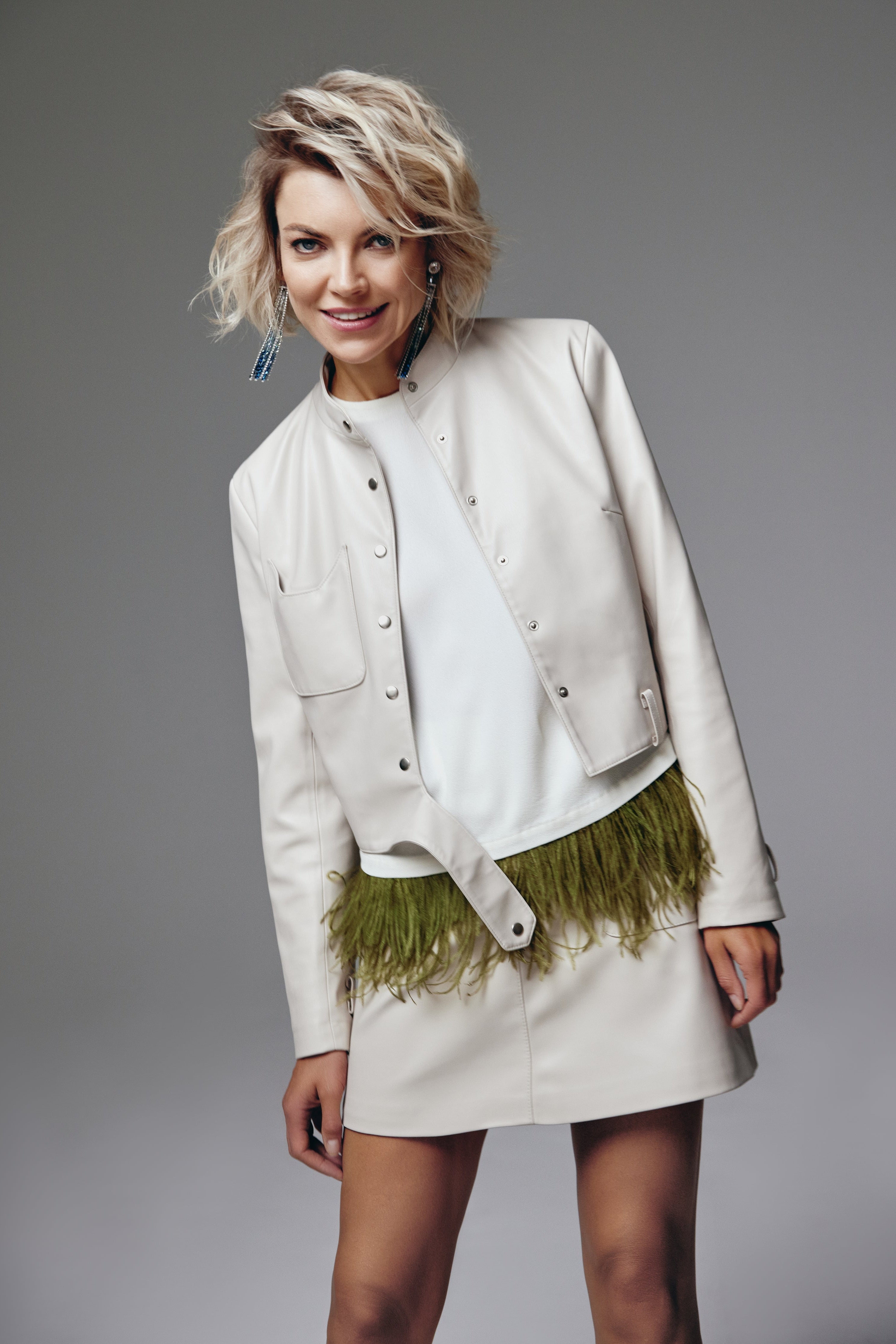Woman wearing a White Catty Skirt from Mimaussy Paris, white jacket with green feather details, on a gray background